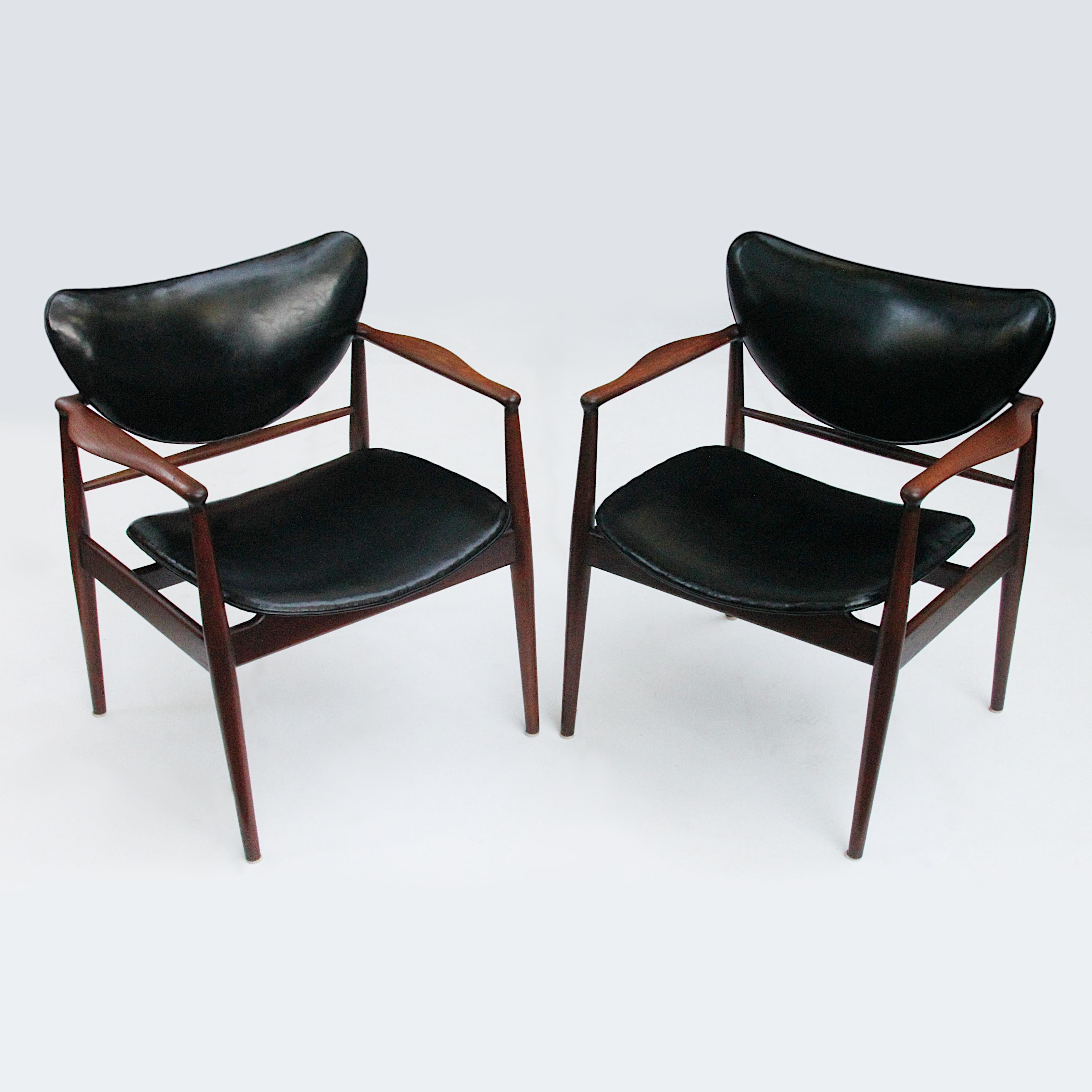 Magnificent pair of Model 48/400 1/2 chairs designed by Finn Juhl for Baker's Modern line in 1952. Chairs feature beautifully sculpted, solid walnut frames and original black vinyl upholstery. These chairs are in remarkable original condition with a