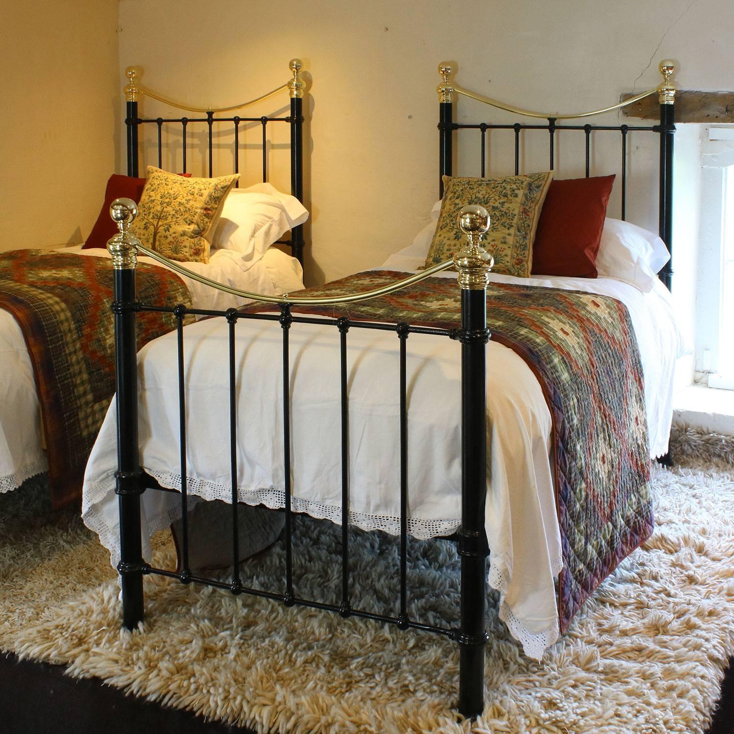 A matching pair of twin brass and iron beds finished in black with curved brass top rails and 2