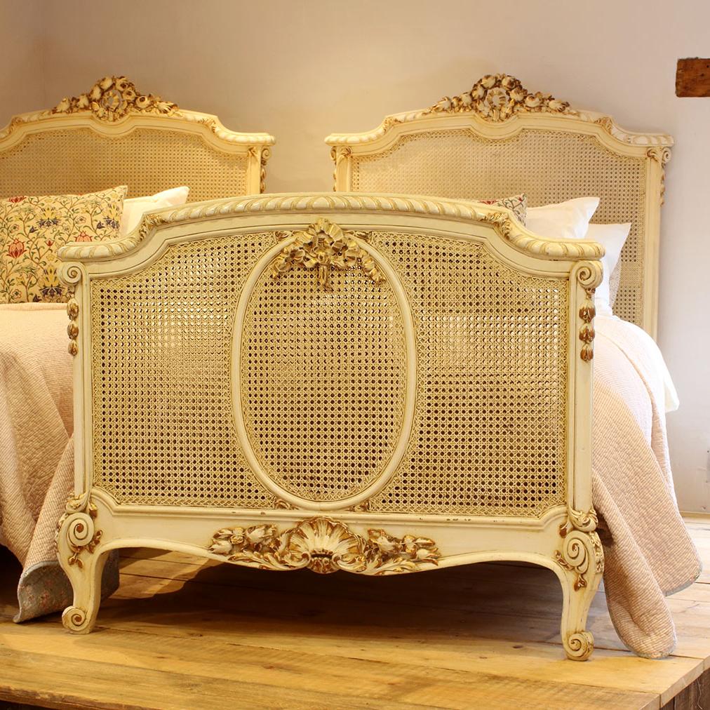 A French matching pair of twin Louis XVI style bedsteads with painted and gilded framework and cane panels. 

These beds accept 3'3