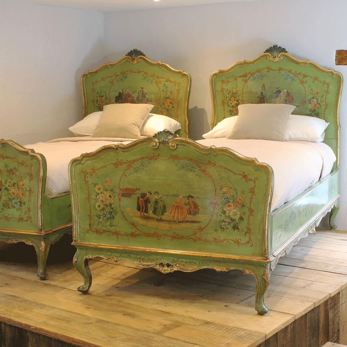 A superb pair of Italian painted single beds in green with gilded highlights and intricate painted scenes depicting characters in a Venetian carnival on the quayside of Venice, flanked by floral designs.

The condition of these beds is in the most
