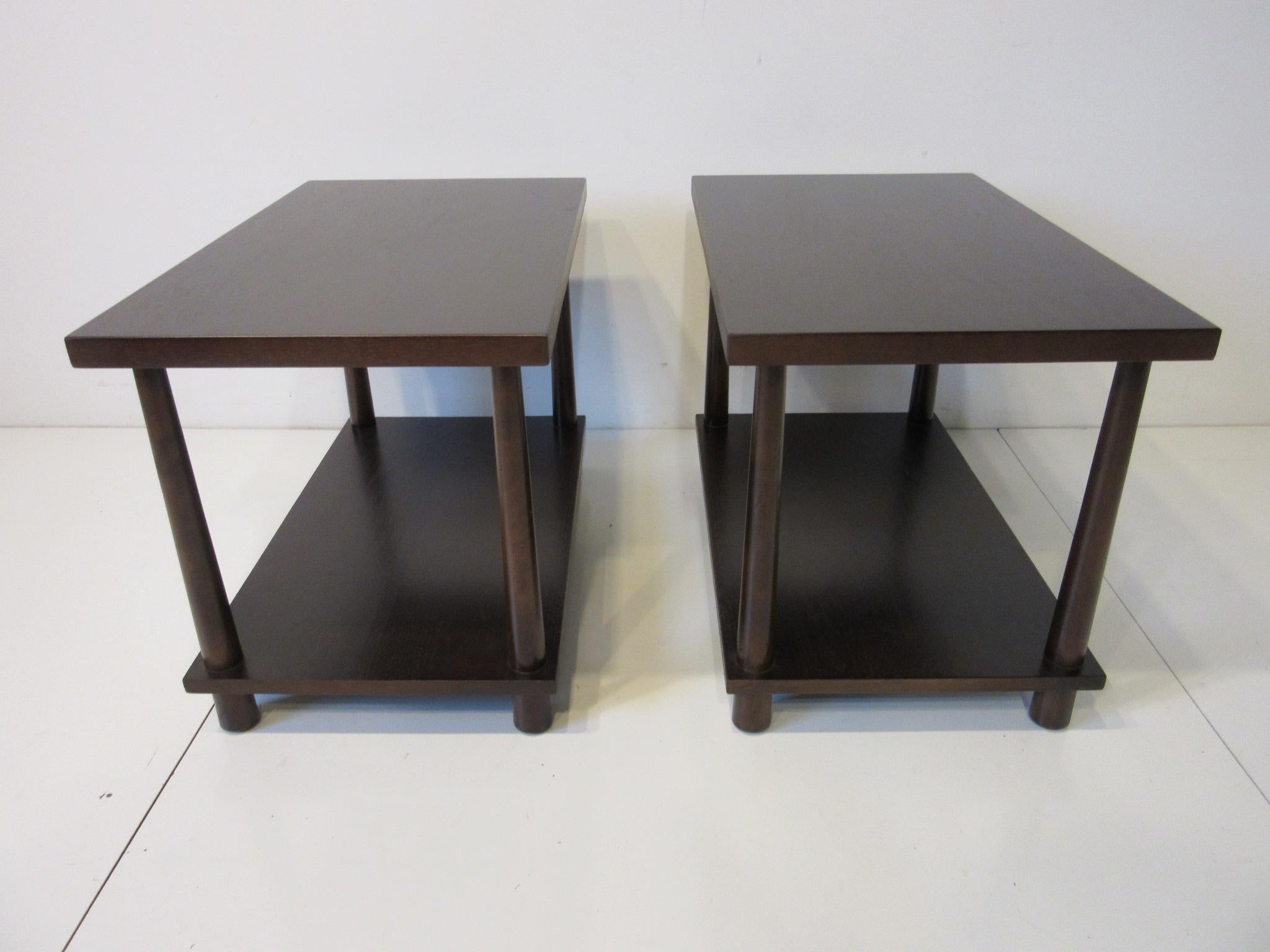 A matching pair of very well crafted double platform end tables / nightstands or side tables with reversed tapered legs in a rich medium ebony toned finish . Retains the manufactures label to the bottom of the table tops by the Widdicomb Furniture