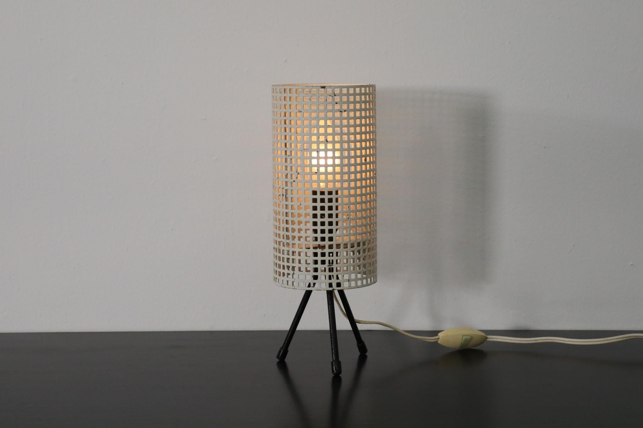 Mid-Century Mategot style table lamp with white perforated cylinder shade and black enameled tri-pod feet for Pilastro. An attractive industrial style table lamp designed by Tjerk Reijenga with sophisticated appeal and ambient light source. In
