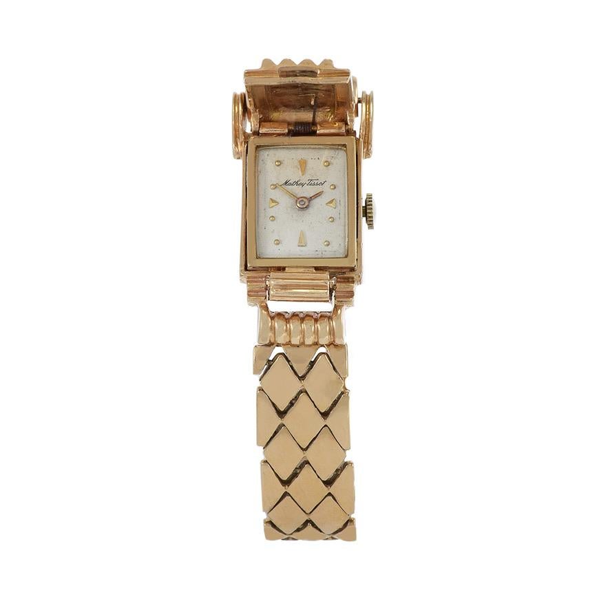 Introducing the Mathey Tissot 1960's 14kt Rose Gold Ribbed Covered Bracelet Watch, a vintage marvel exuding timeless elegance and sophistication. This exquisite timepiece features a distinctive rectangular flip case adorned with ribbed detailing,