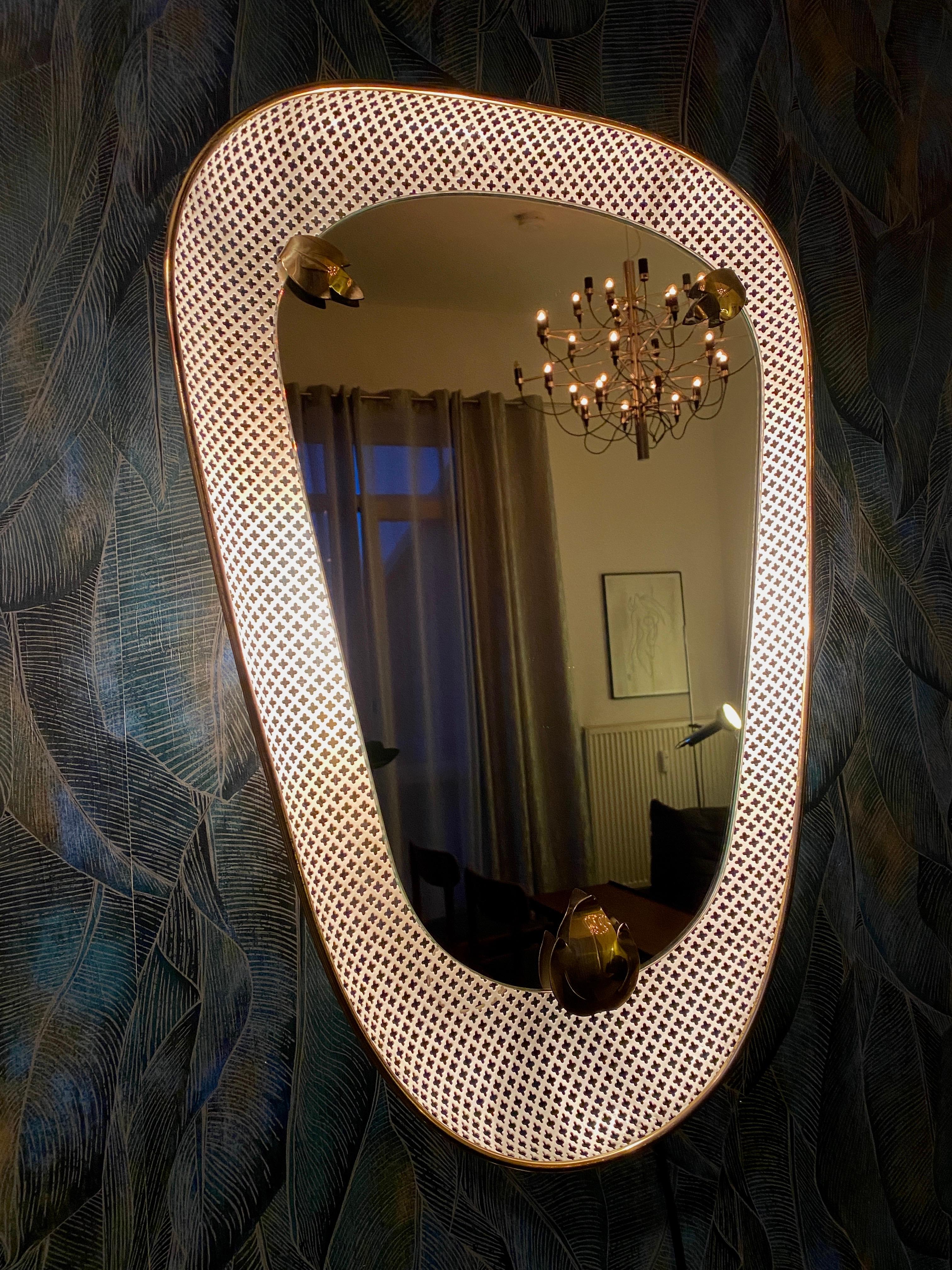 A wall mirror with indirect lighting by Mathieu Mategot. It was made in the 1950s.
Inside the frame are two E14 light bulbs (max. 40W).
A push button switch is located at the bottom of the mirror.
The frame is made of white perforated sheet metal in