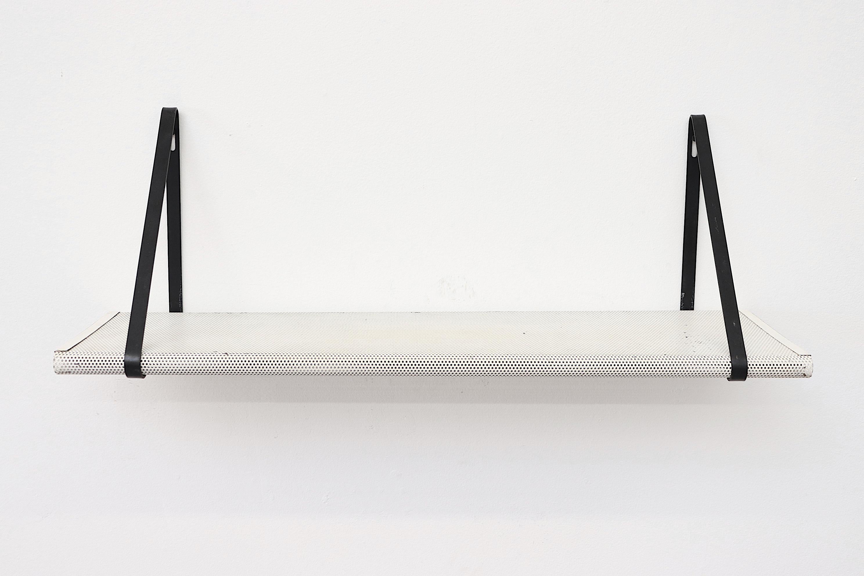 Made in the 1950s and 1960s, this a rare Mathieu Mategot wall-mounted Industrial book shelf is constructed of white enameled perforated sheet metal with black metal key-slotted band mounts. In original condition with visible wear and some enamel