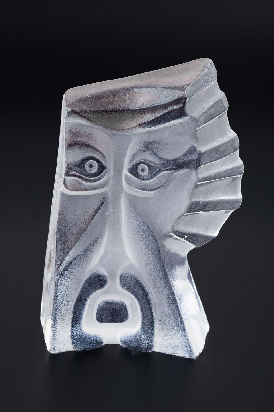 Mats Jonasson pour Målerås Glasbruk. Sculpture en cristal de la série Masqot Shama.
La pièce représente un visage stylisé, où les surfaces claires et givrées interagissent pour créer de la profondeur et un jeu de lumière saisissant dans le motif