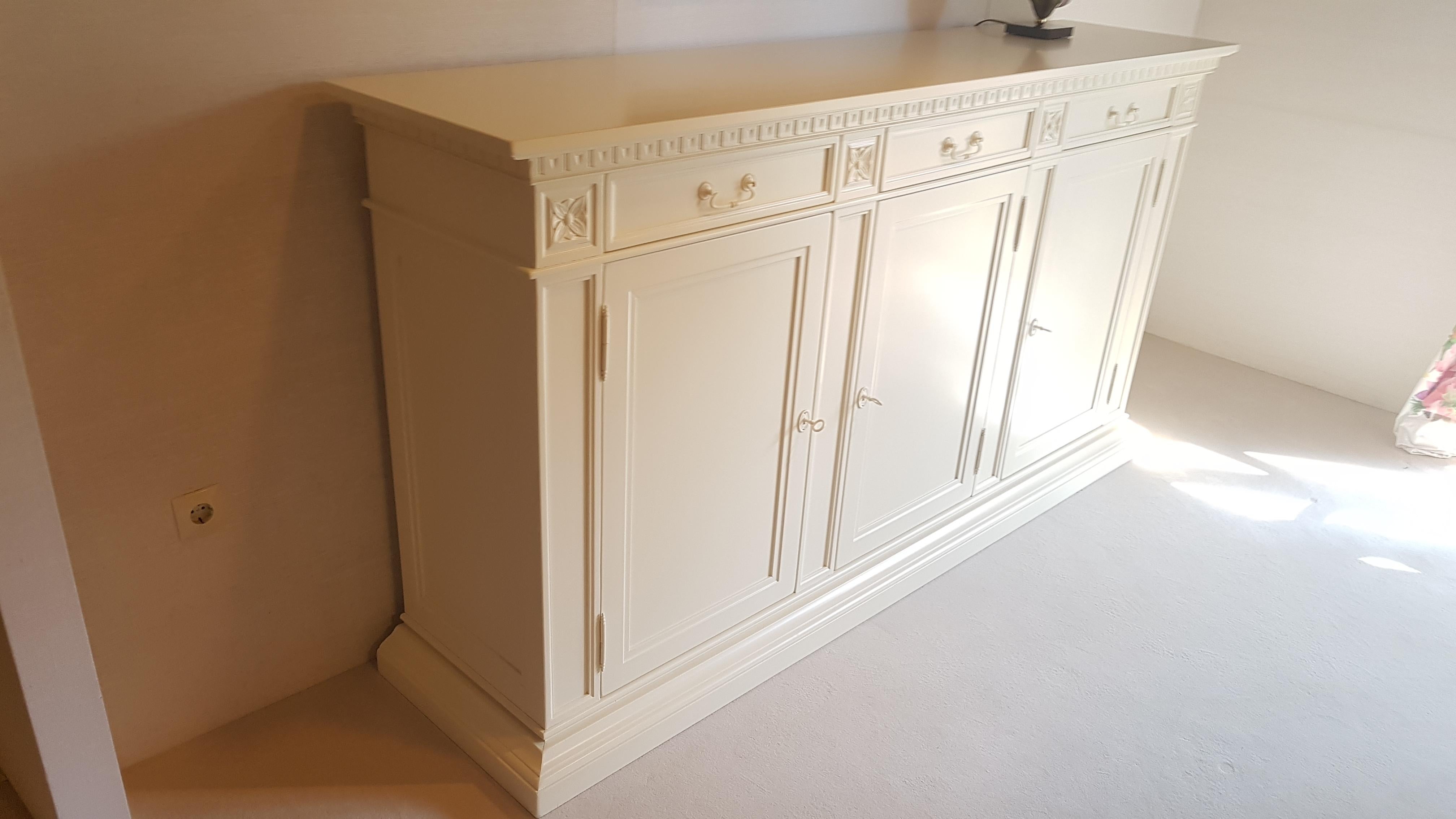 Beautiful matte white or old white buffet with a classic design. Offers antique style ornamentations finished with a high quality matte white paintjob. With finely crafted brass handles and three lockable doors. With an interior shelve and three