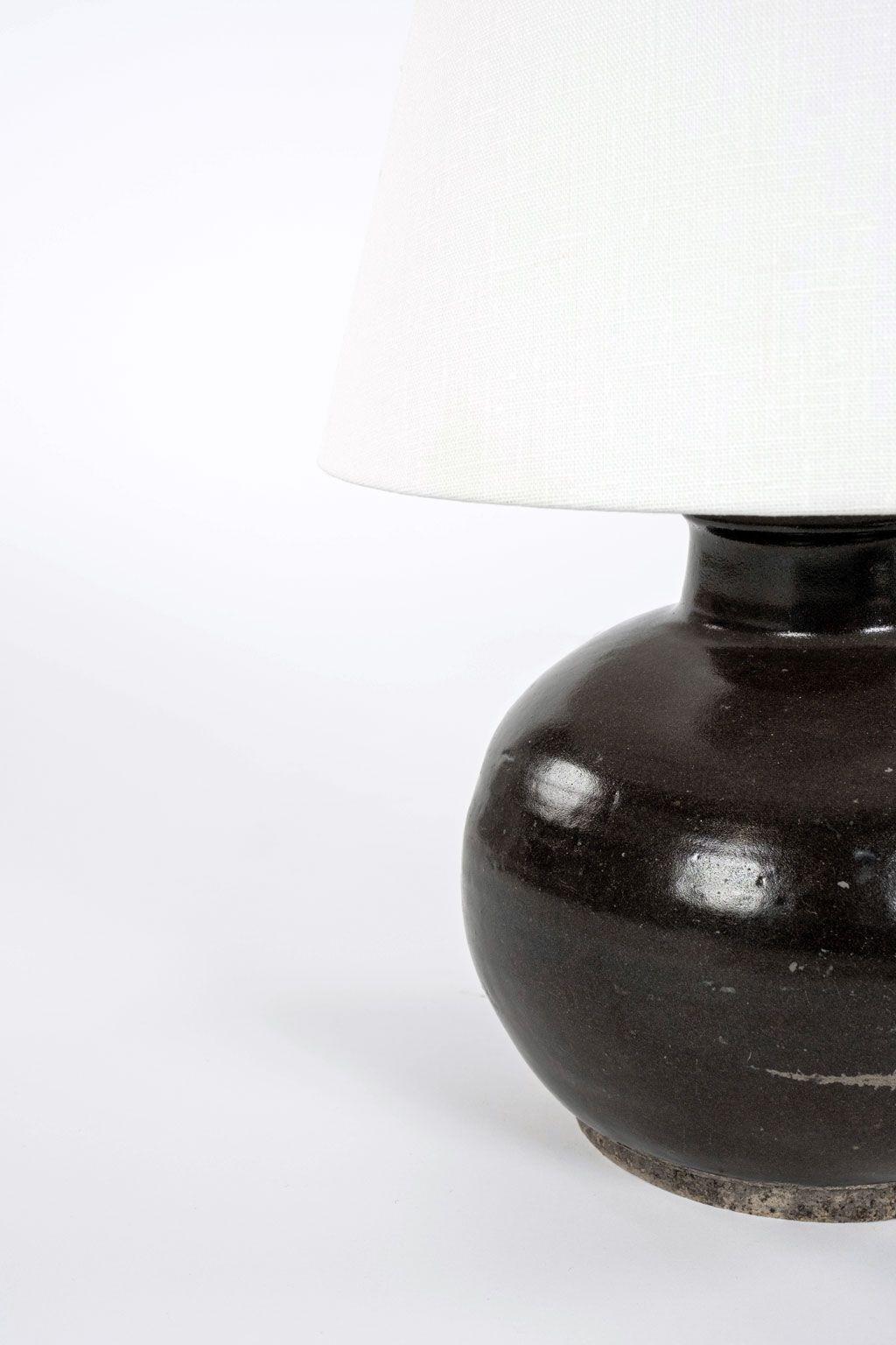 Matte dark brown glazed lamp from antique Chinese oil jar. Newly-made custom lamp from lamps made with antique Chinese oil storage jar. Natural-color terracotta footed base. Newly wired for use within the USA. Includes white linen shallow drum uno