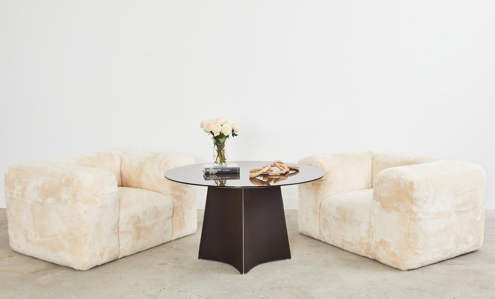 Chic Italian leather and glass round dining table or center table designed by Rodolfo Dordoni for Matteo Grassi. The pedestal style table features a winged base clad in leather with zippers on the border that fit like a fine Italian suit. The base