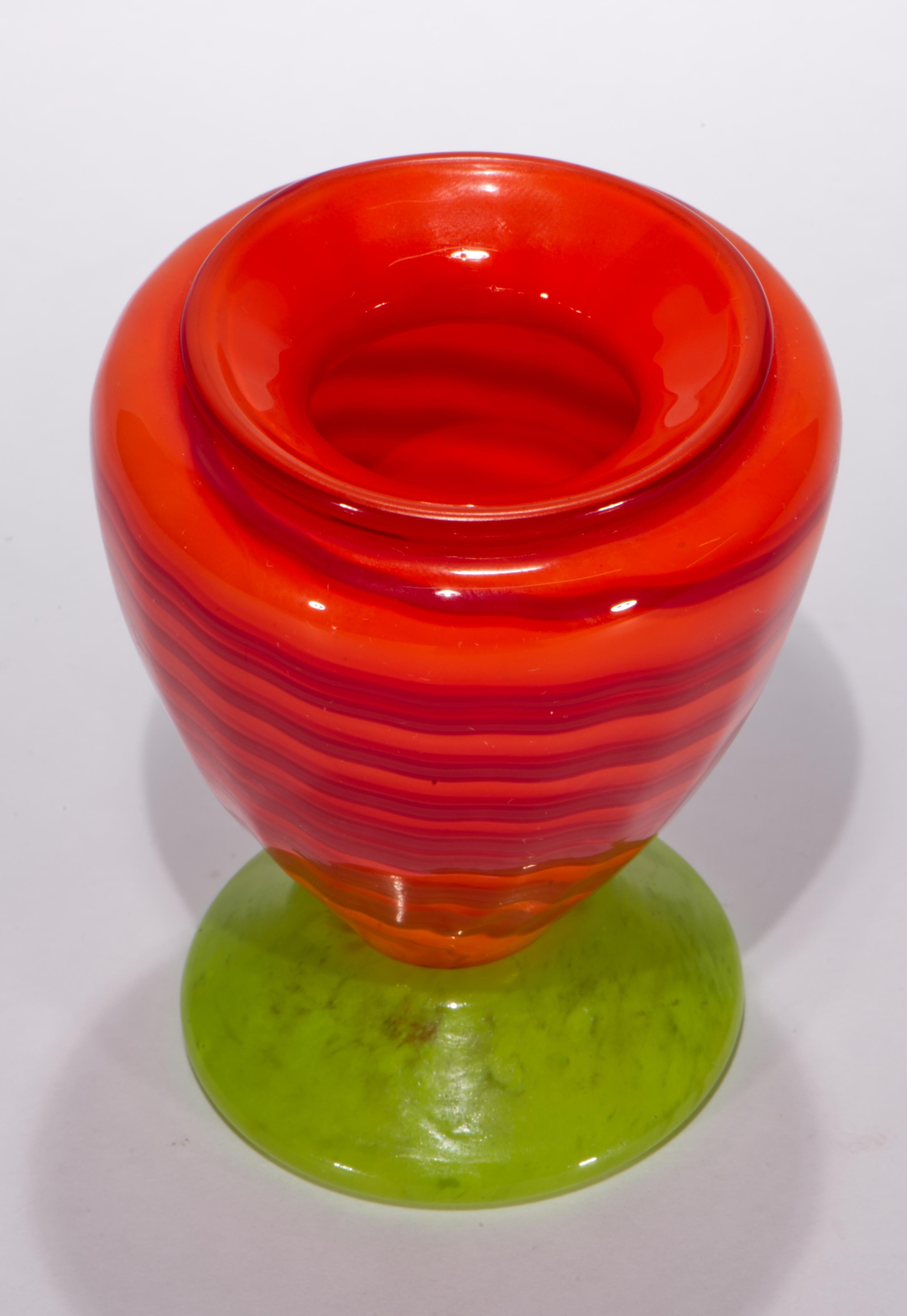 Il vaso di gemme in vetro artistico vintage presenta un corpo arancione con accenti di nastro ondulato in vetro fuso rosso; il vetro colorato è stratificato e racchiuso in uno strato di vetro trasparente con la tecnica del sommerso. Il corpo a forma