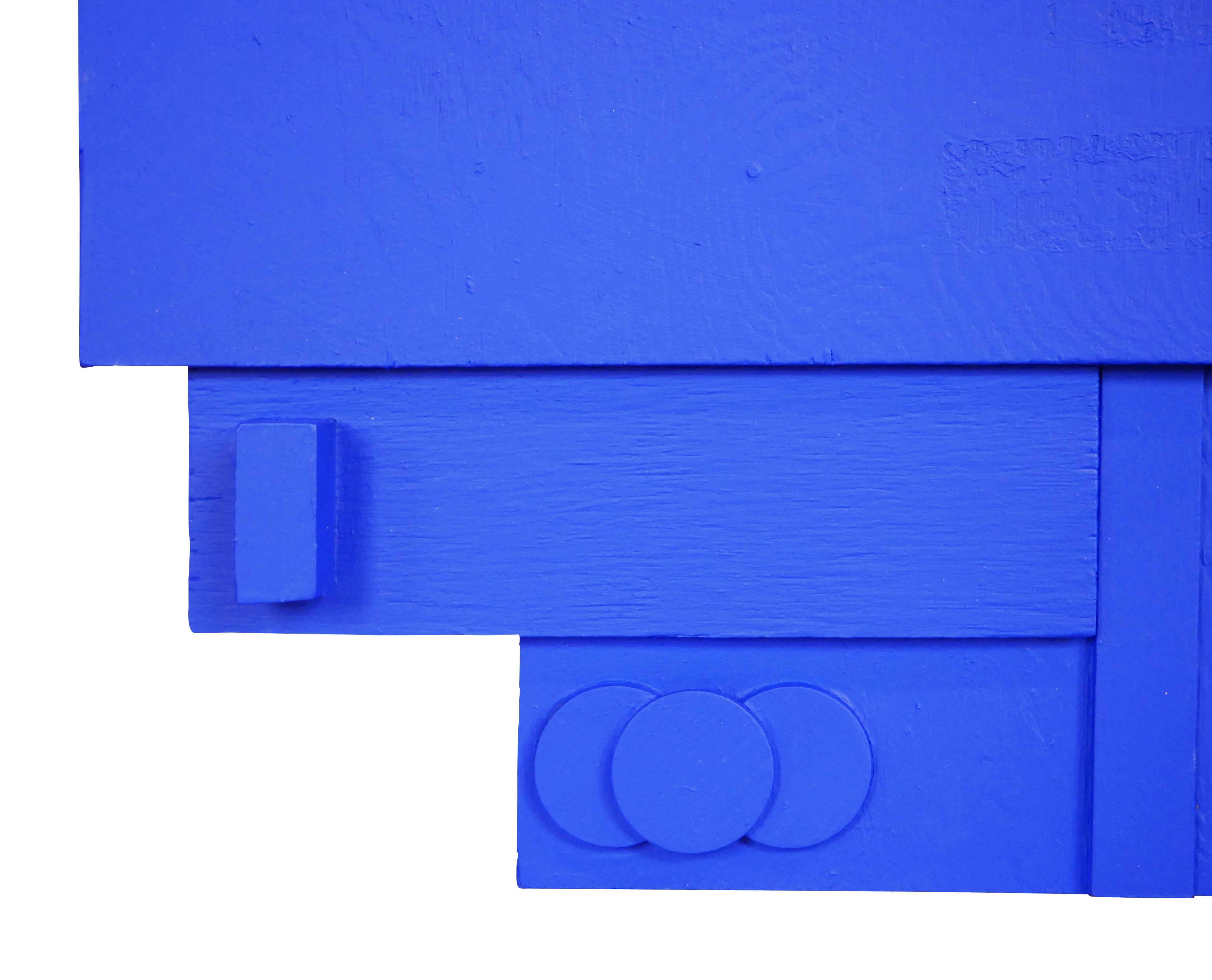 Abstract wall sculpture featuring three dimensional geometric shapes painted with bright blue paint. The uniqueness of this blue does not derive from the ultramarine pigment, but rather from the matte, synthetic resin binder in which the color is