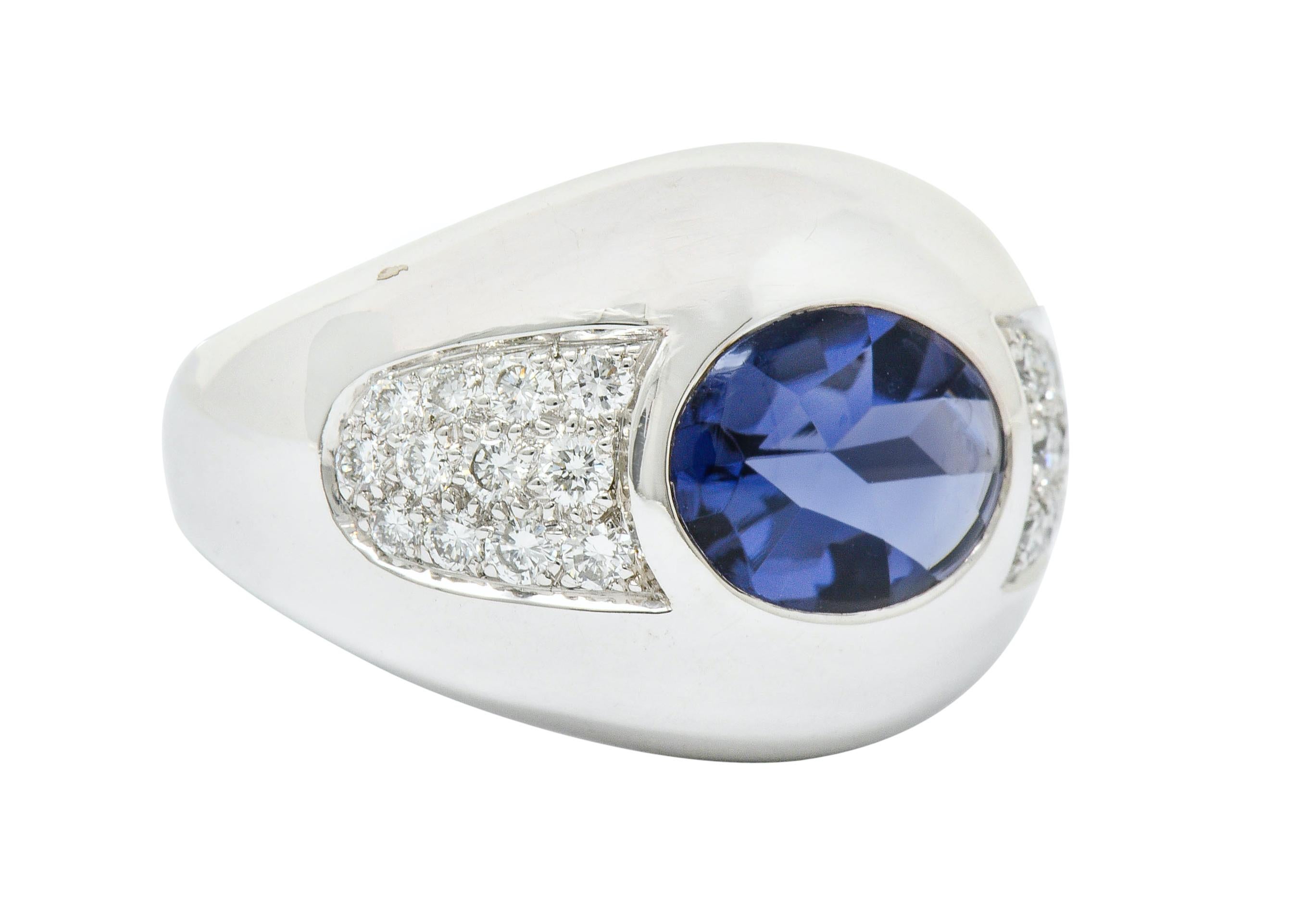 Bombay band ring centering an oval buff top iolite measuring approximately 10.5 x 8.3 mm

Transparent and brightly violet in color

Flanked by two pavè fields of round brilliant cut diamonds weighing approximately 0.65 carat; F/G color and VS