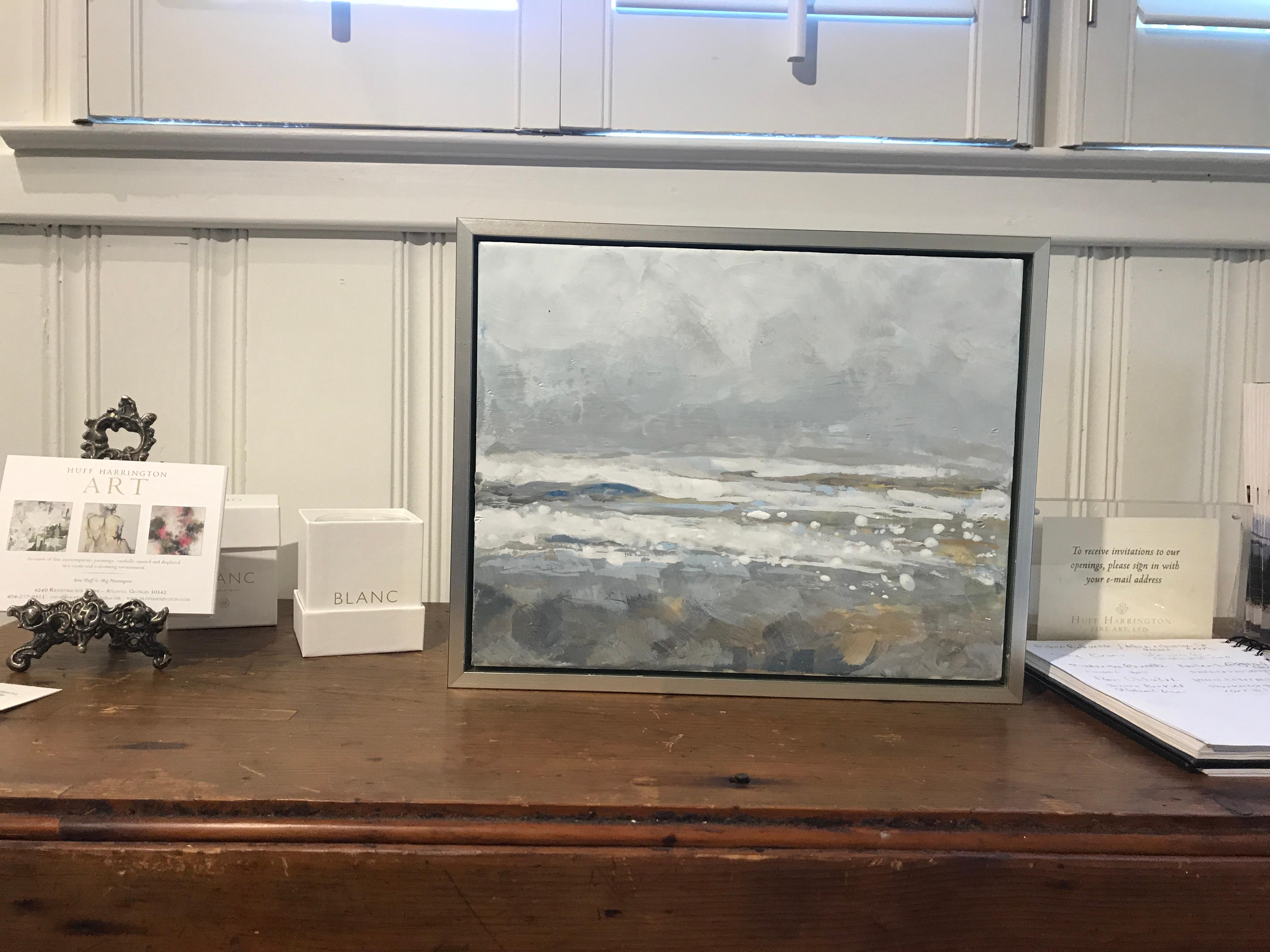 'Salt Tipped' is a small silver framed abstract encaustic on board seascape painting created by American artist Maureen Naughton in 2019. Featuring a delicate palette made of grey, white, brown, gold and soft blue tones, the painting, leaning