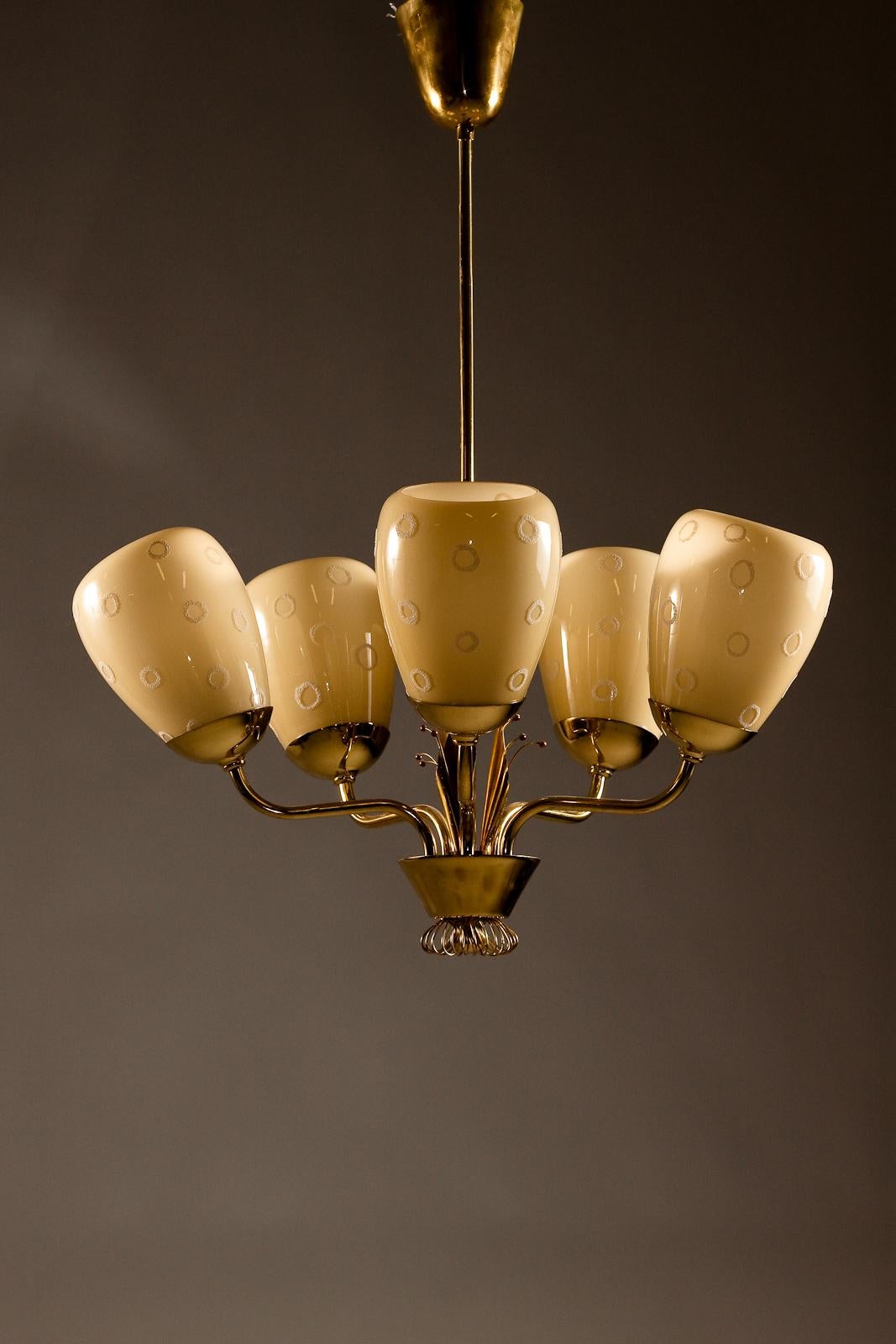 Introducing the stunning Mauri Almari 1950's brass chandelier from Idman Oy. This vintage beauty features intricate decorative ornaments in brass, adding a touch of elegance to any room. The hand-painted glass shades exude a warm, inviting glow,