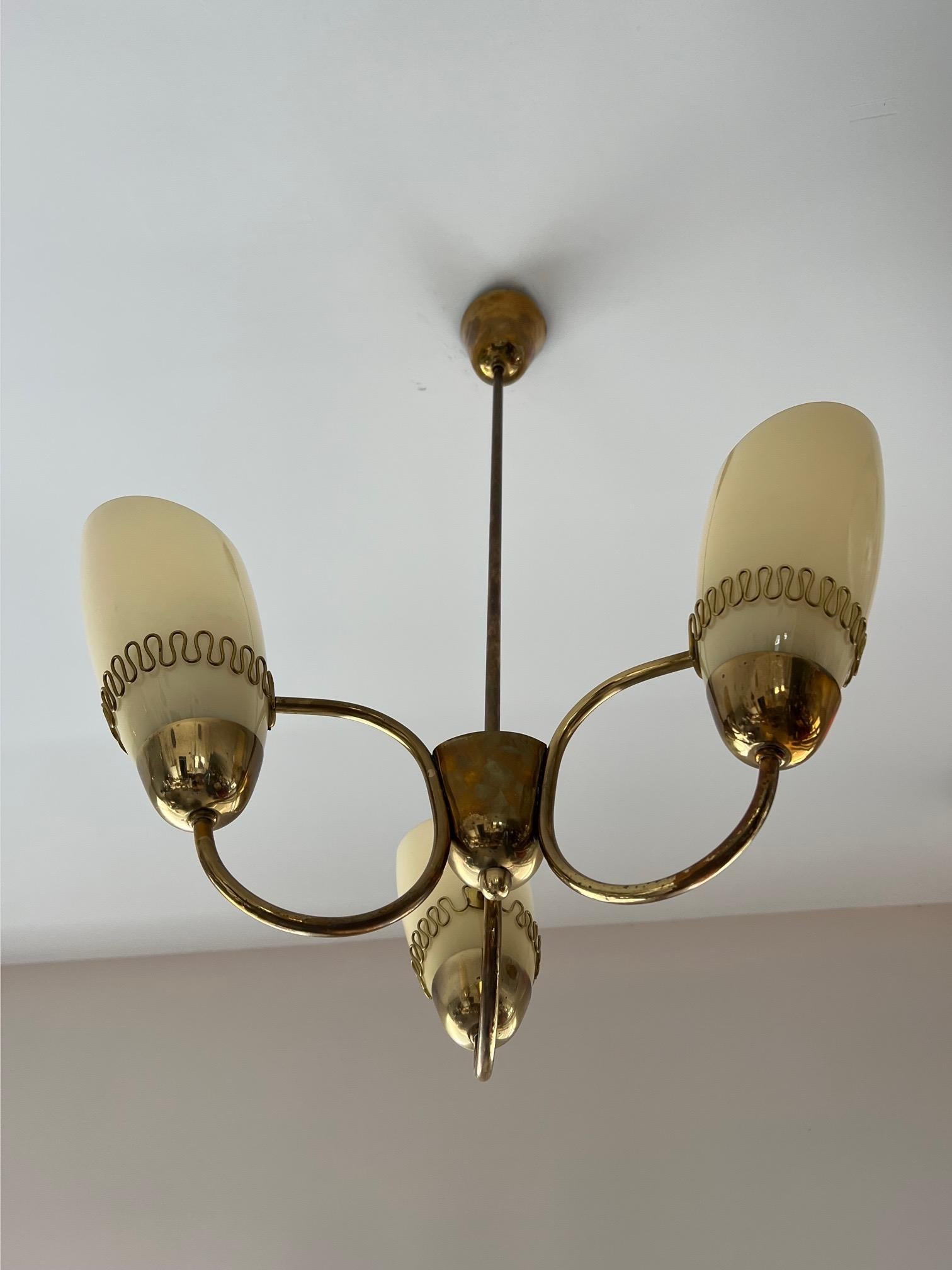 An elegant three arm chandelier by Mauri Almari for Idman (model K1-44). Signed twice. Brass with opaline beige shades.


