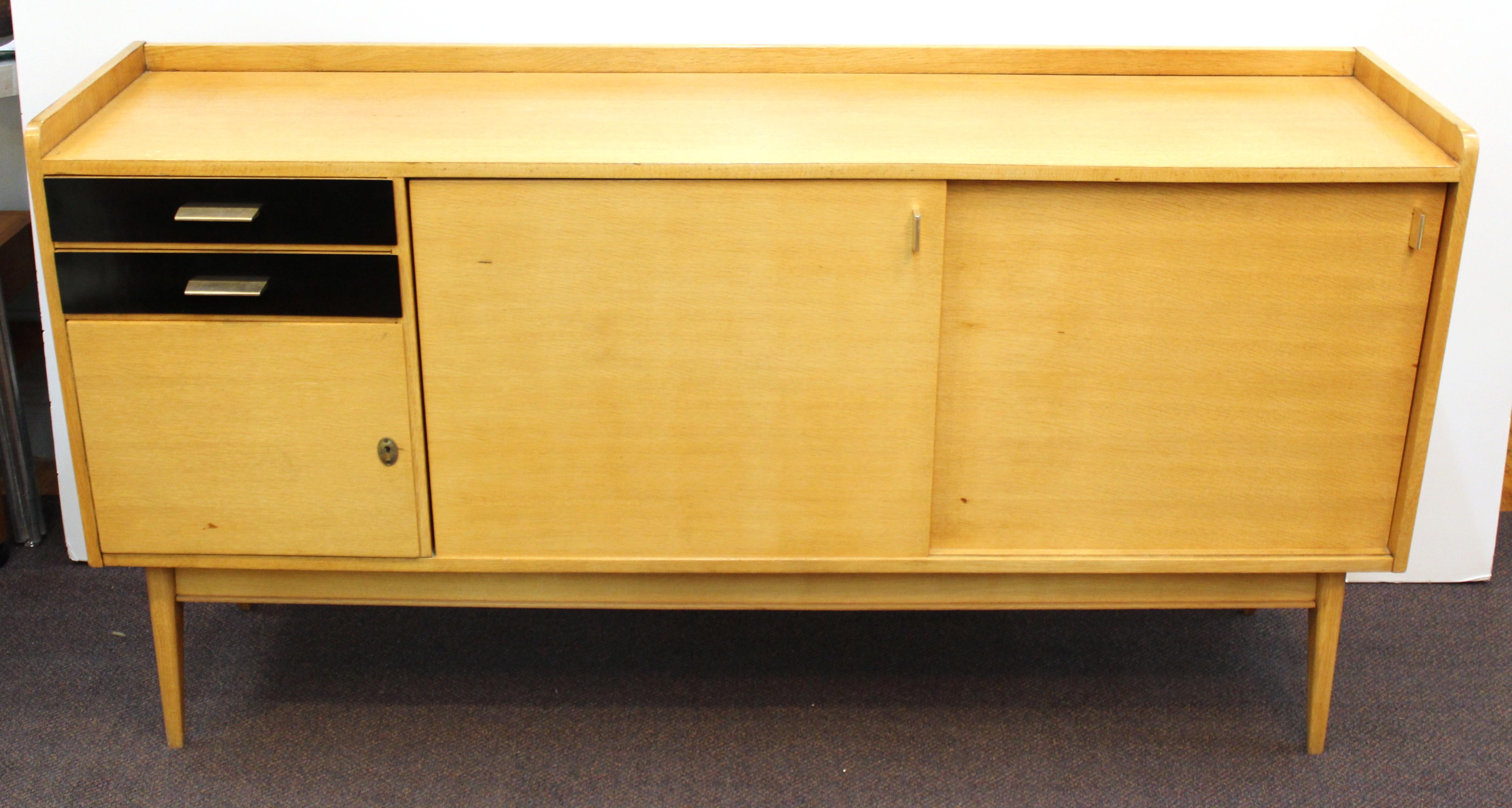French Mid-Century Modern oak credenza or sideboard, designed by Maurice Pre, with two stacked drawers at the left side over a door and two sliding doors at the right, the sideboard raised on four splayed legs. The piece has a maker's label