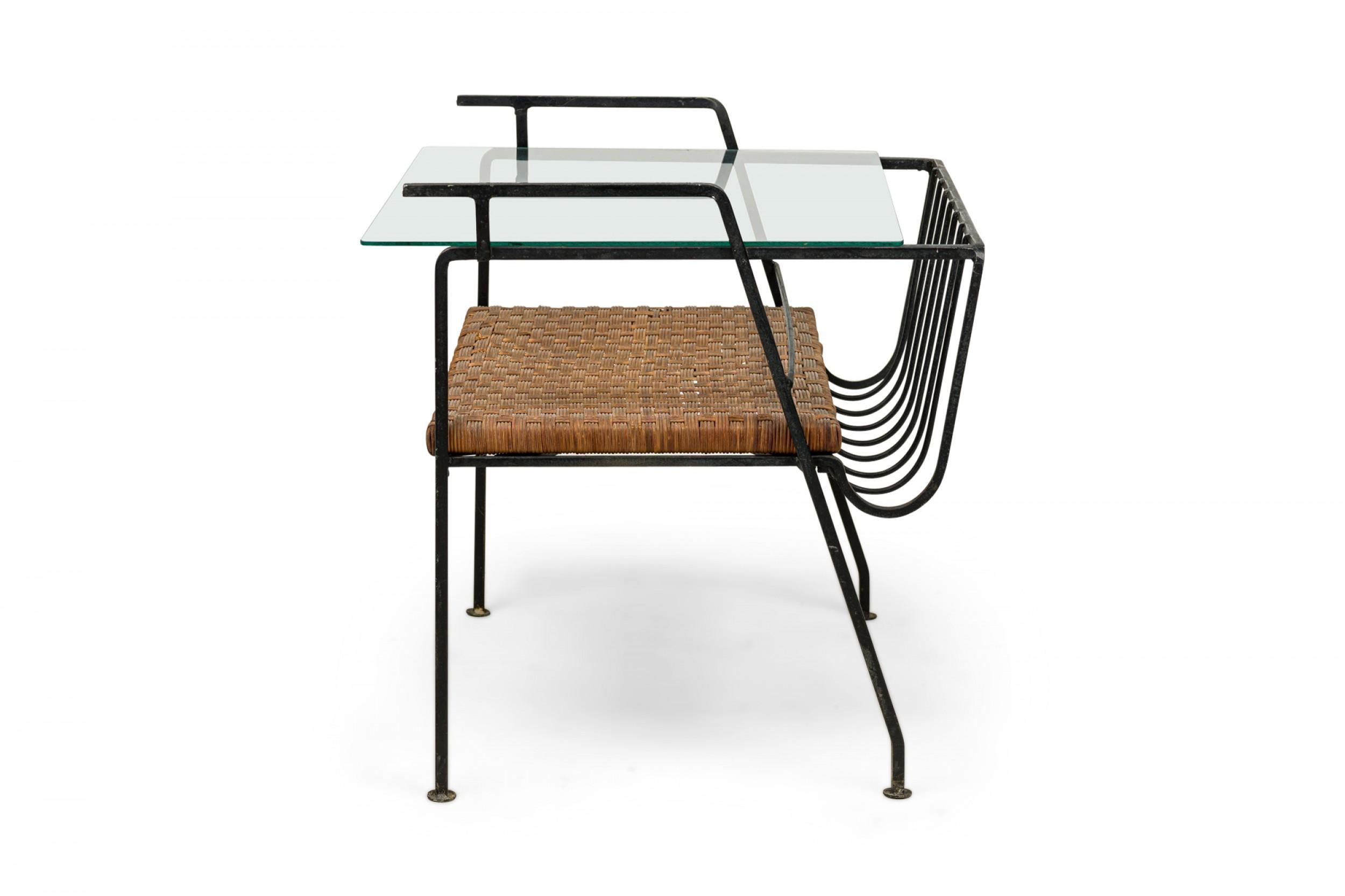 Mesa auxiliar revistero rectangular de metal, de dos niveles, de mediados de siglo, con respaldo calado que se inclina suavemente hacia arriba para alojar revistas, con estante inferior de ratán tejido y tapa de cristal transparente. (MAURIZIO