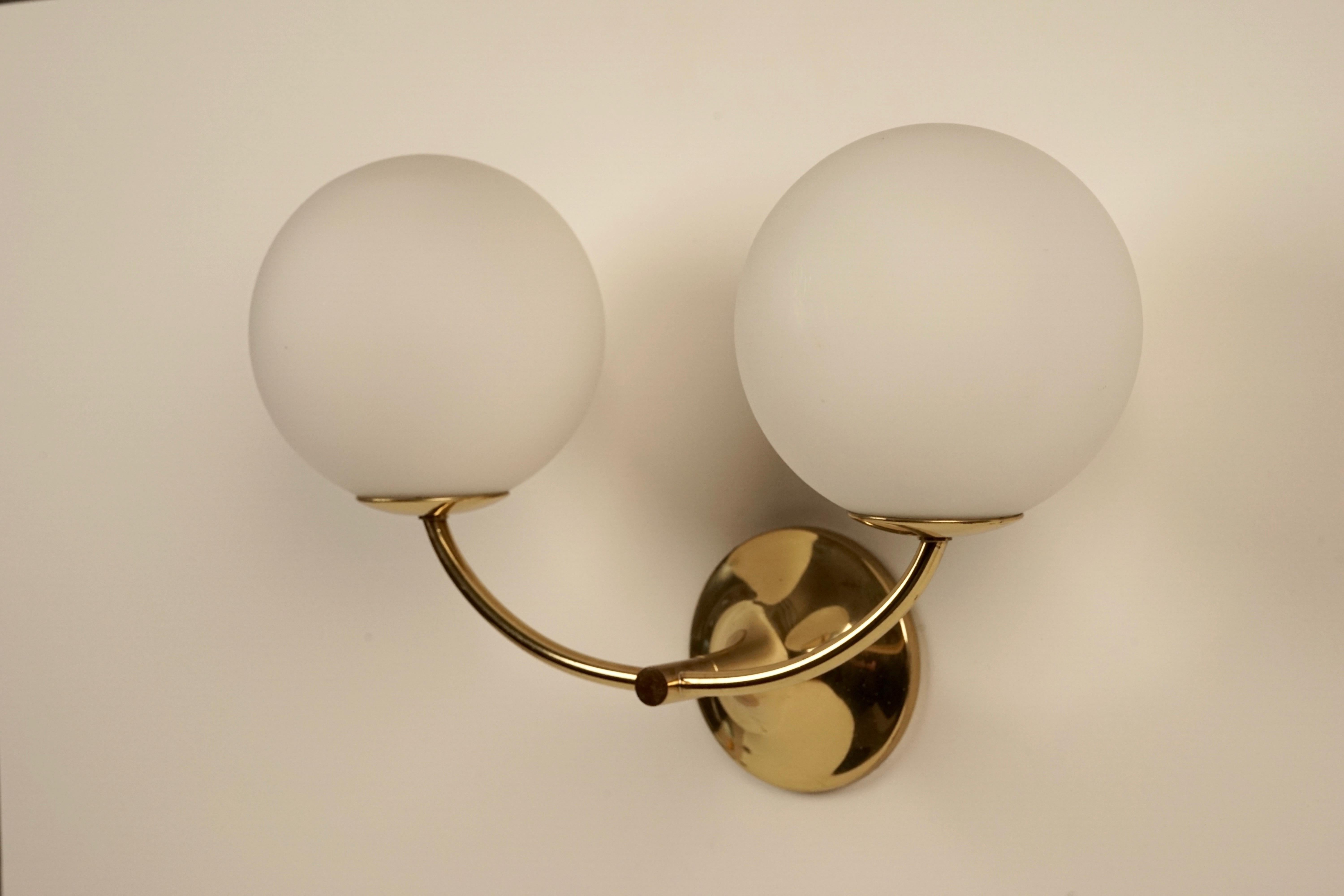 A Max Bill wall lamp composed of two hand blown opaline glass globes mounted on an elegant brass body.
The globes are fitted with metal threads which enable easy removal.