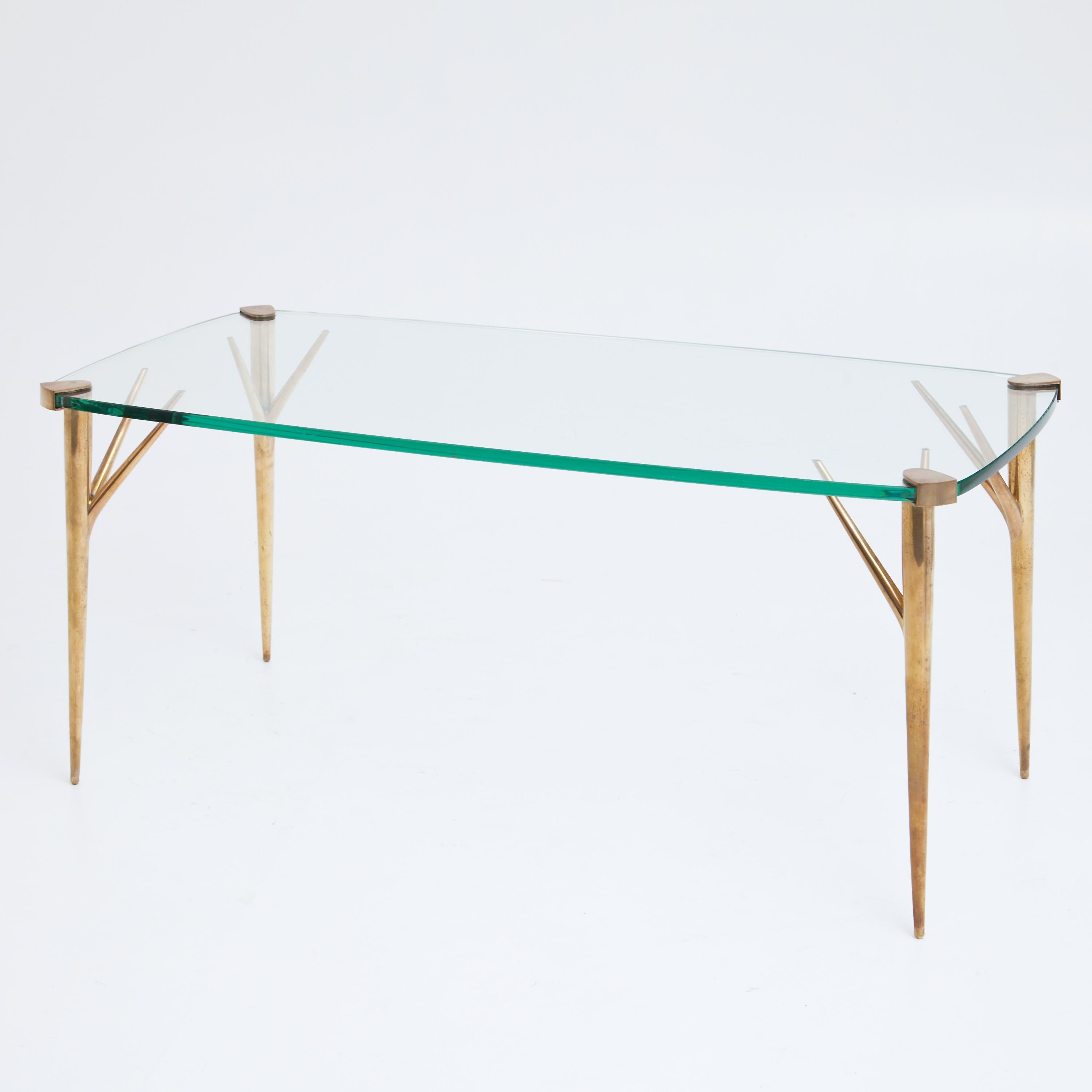 Coffee table on four forked brass legs supporting the slightly rounded glass top. The table was designed in 1956 by Max Ingrand for Fontana Arte.