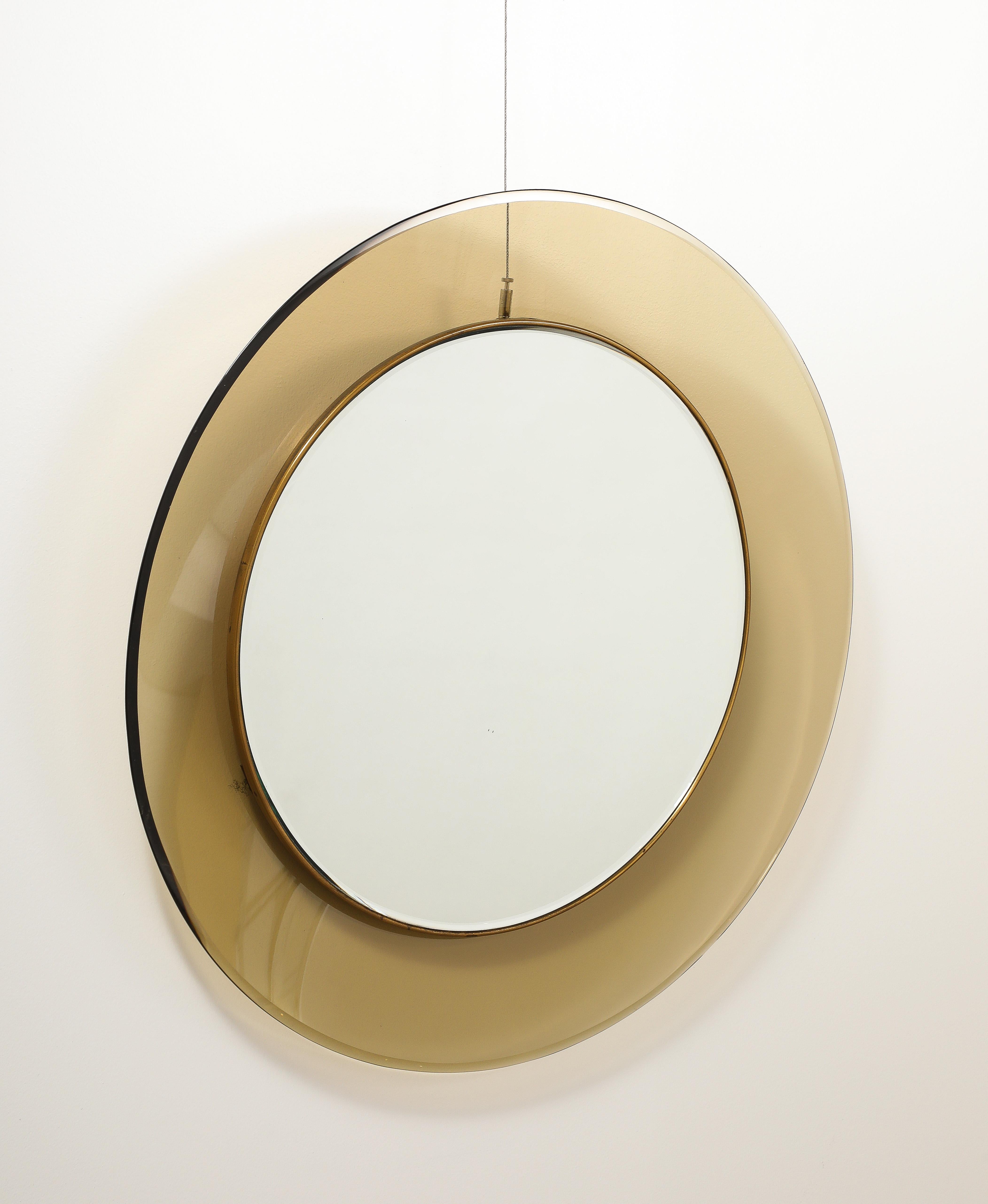 Max Ingrand, pour Fontana Arte Modèle '1699' miroir mural circulaire en verre teinté fumé élégant avec un miroir rond en verre clair monté au centre, entouré d'une moulure en laiton.  La coloration du verre fumé et coloré, le laiton merveilleusement