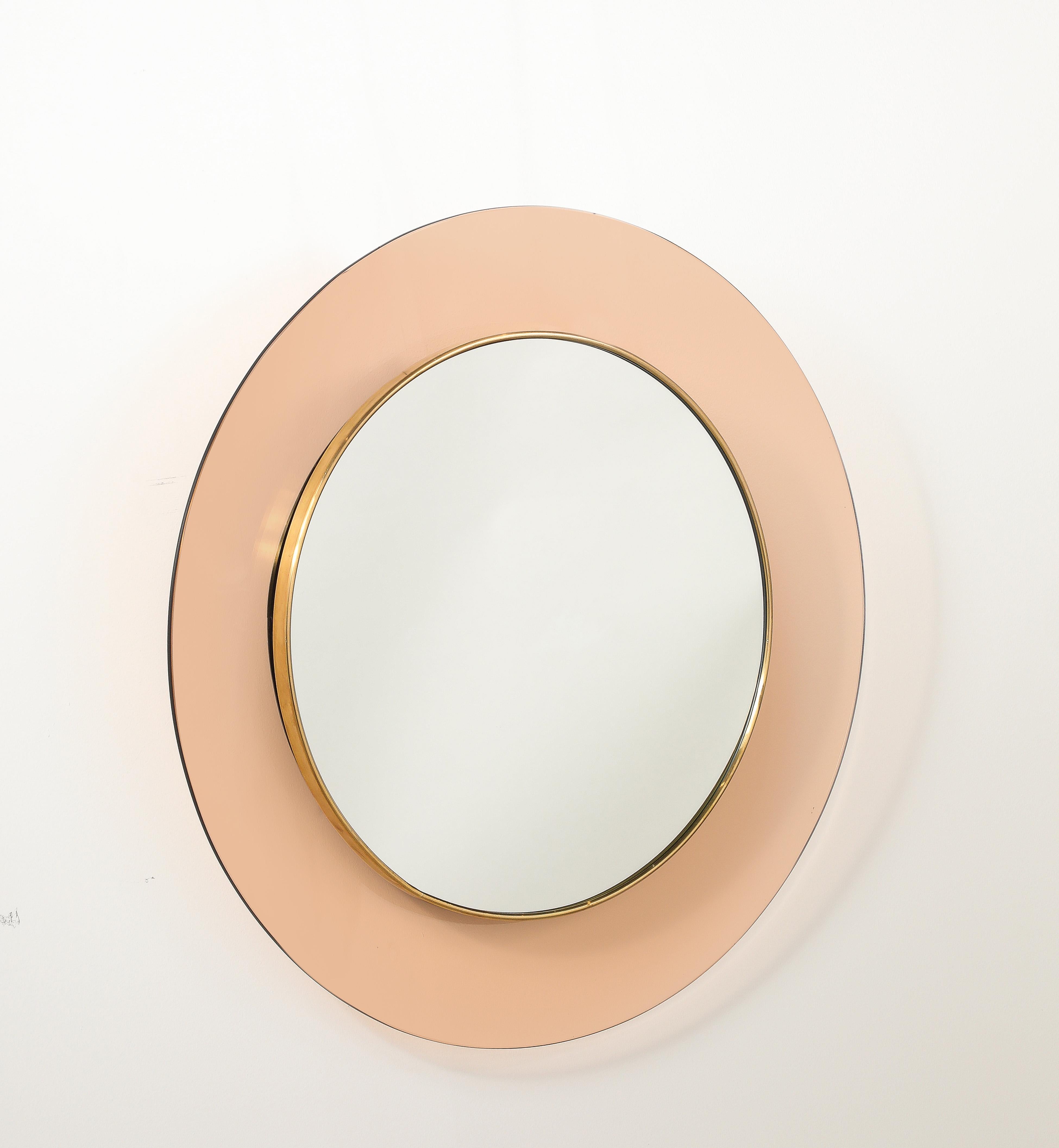 Max Ingrand, pour Fontana Arte Miroir mural circulaire modèle '1699' en verre teinté rose avec au centre un miroir rond en verre transparent, entouré d'une moulure en laiton.  La coloration du verre rose et du laiton avec une patine magnifique et le