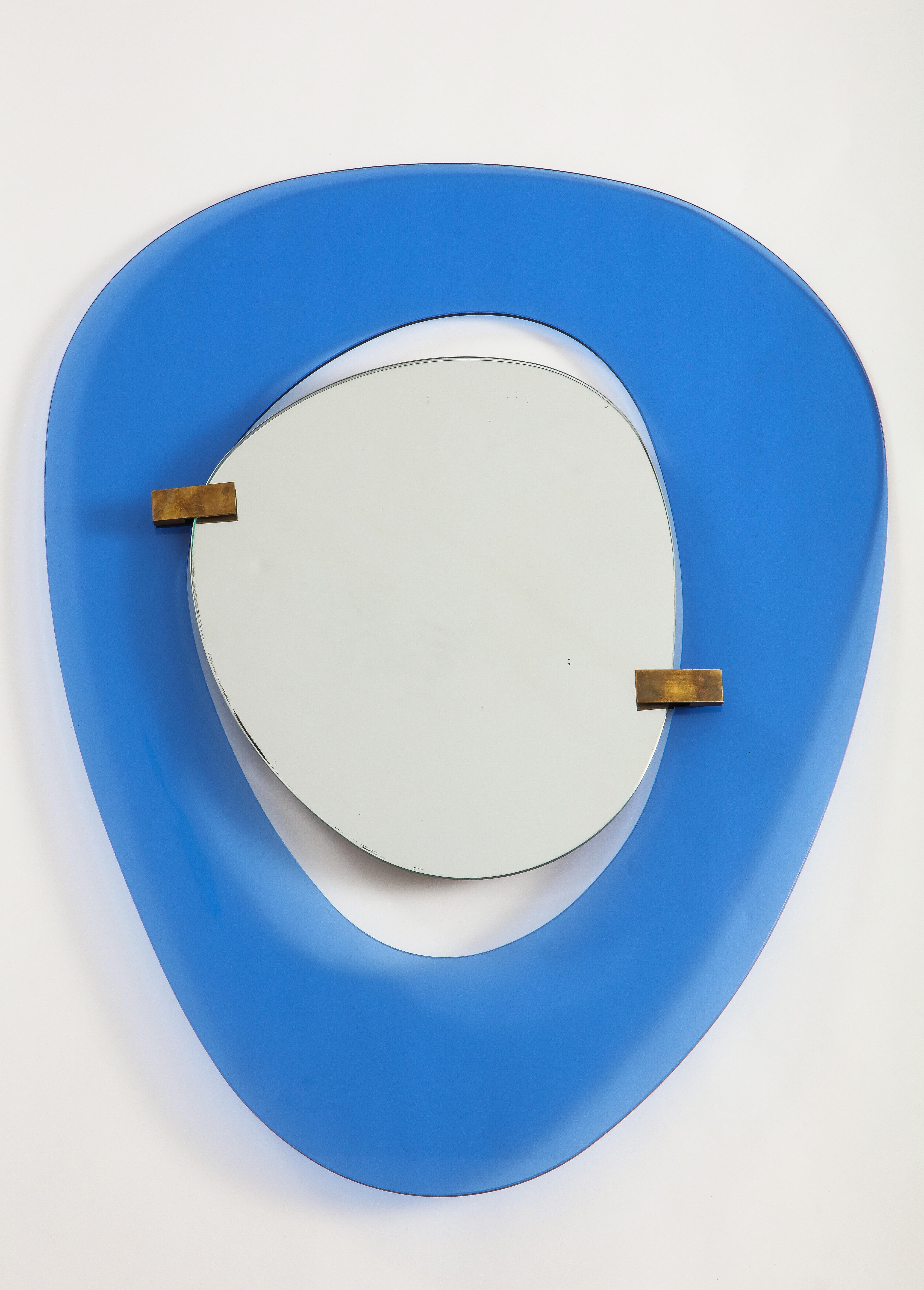 Max Ingand for Fontana Arte rare sculptural mirror with asymmetrical blue polished glass frame surrounding floating mirror which is attached with two brass clasp mounts.

Literature:
Edoardo Paoli, L'importanza dello Specchio, Milan, p.