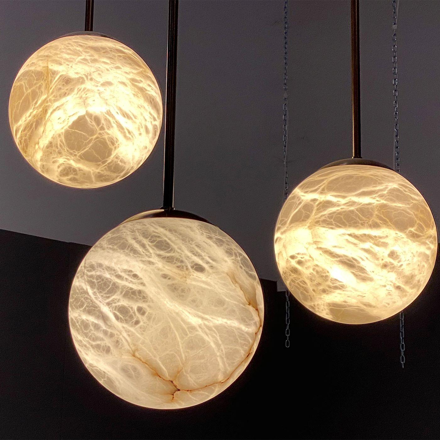 Maxi Alabaster Moon pendants, in a set of three, recall the magic of full moon nights. Large, illuminated globes that float in the air and emit a warm and diffused light. Alone or in a composition, these pendants reveal the vibrant richness of