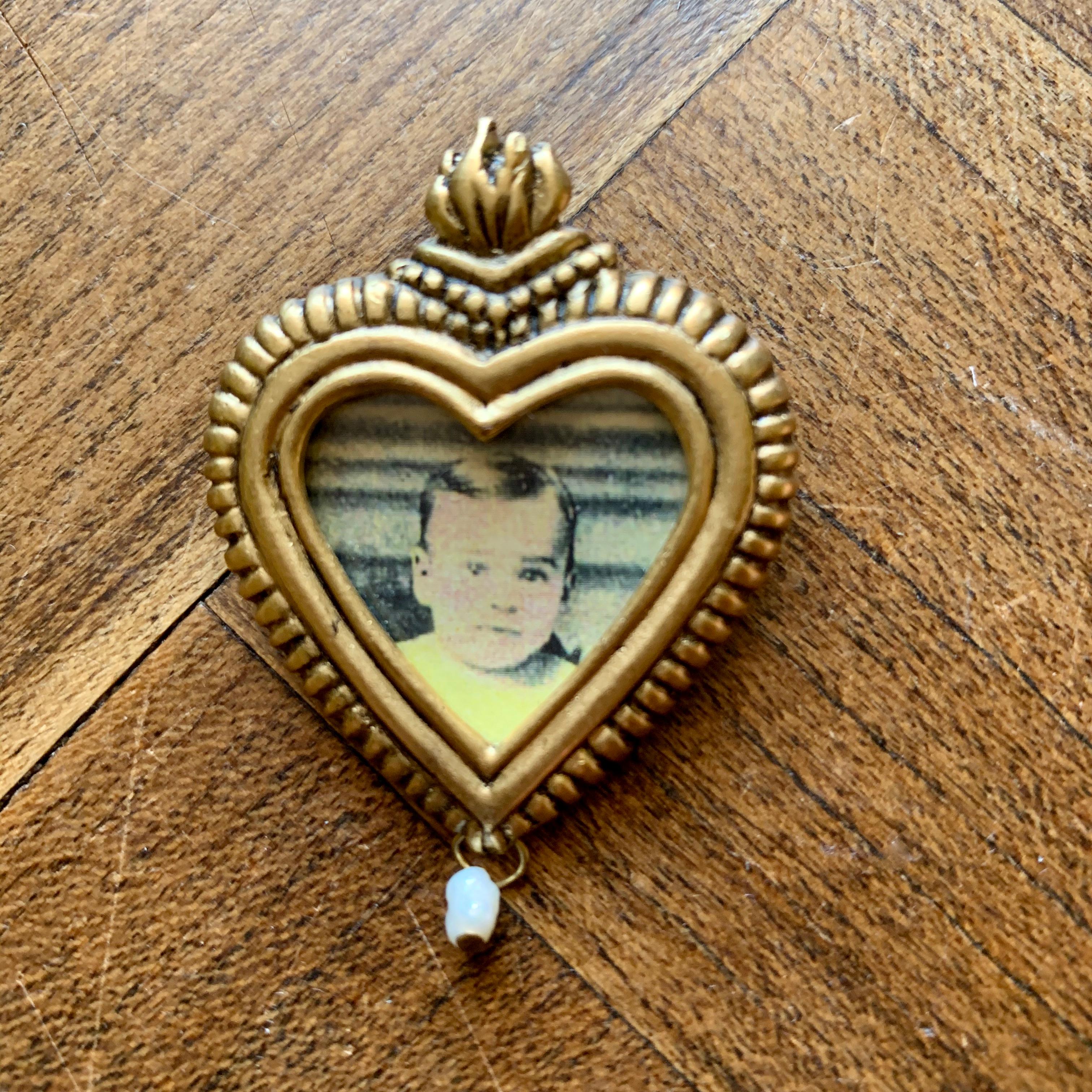From John Wind's Maximal Art 1980s jewelry collection, a portrait pin molded as a sacred heart.

The cast metal heart shaped picture holder has a molded flame at the top and a dangling seed pearl at the bottom. Shown with a place holder picture of