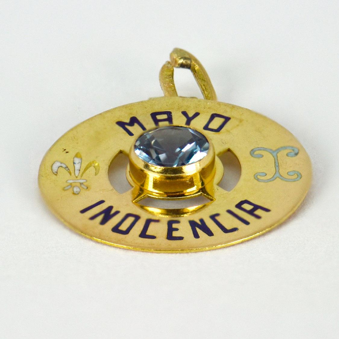 An 18 karat yellow gold charm pendant designed as a gold disc with enamel inlay of 'MAYO INOCENCIA' (May Innocence) with the zodiac symbol for Gemini and the fleur de lis depiction of a lily (meaning perfection or light) in enamel, and set to the