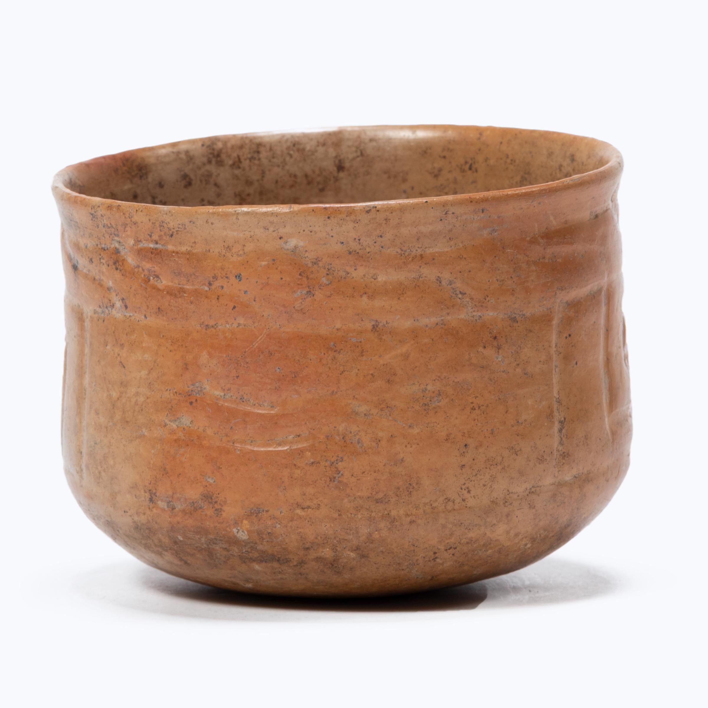 With a beautifully worn, glossy finish, this petite orangeware bowl is a wonderful example of Maya pottery. The delicate bowl is etched with a geometric patterns and coated in a layer of clay slip for a light orange finish. Exposure to combusted