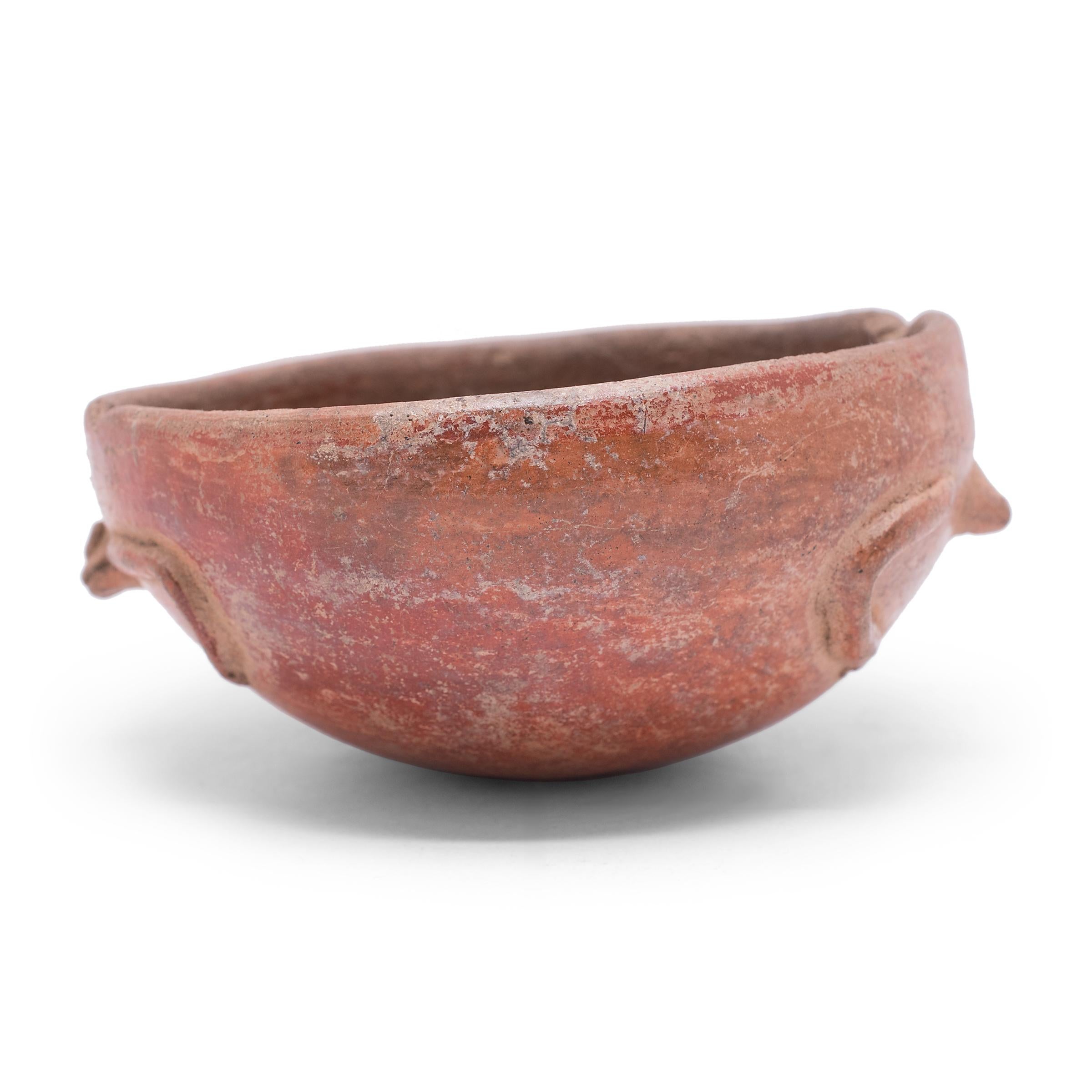Exhibiting a rich patina, this petite redware bowl is attributed to Maya culture and shows many telltale signs of Pre-Columbian pottery. Speckled with imperfections, the vessel's warm red-orange coloration was achieved by applying a mineral-rich