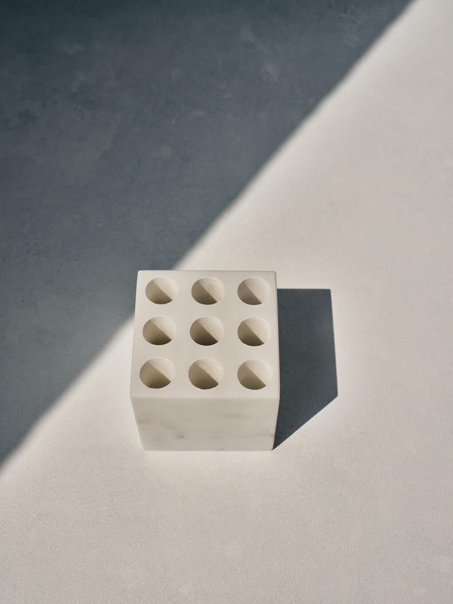 Maya square holder by Faye Tsakalides. 
Dimensions: 8 W x 8 L x 8 H cm
Materials: White Dionysius marble.
Technique: Crafted from a single piece of marble. Hand-crafted, Polished. Mat finished. 

Faye Tsakalides is a Greek architect and