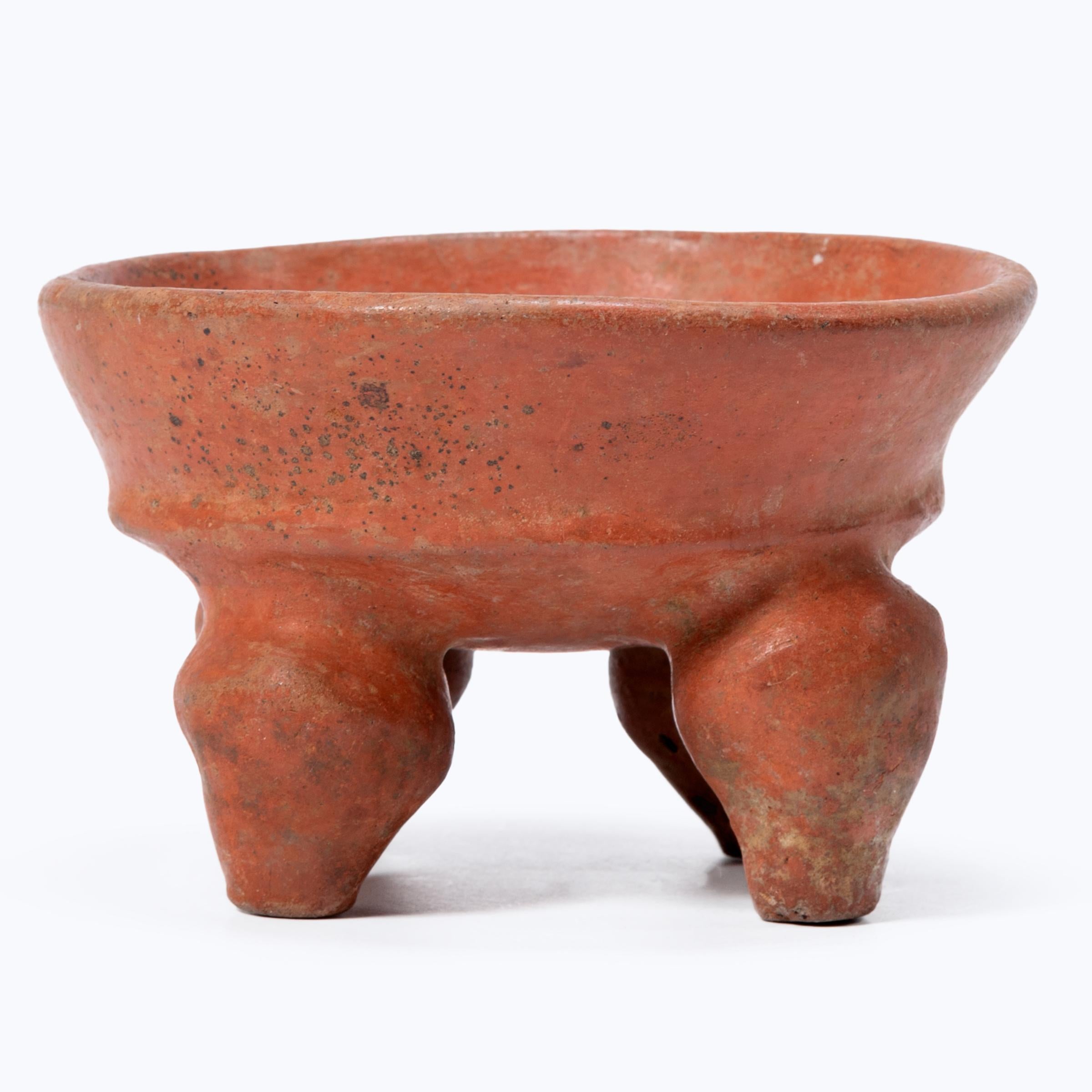 This wide-mouthed bowl raised upon four bulbous feet is formed in the style of mammiform tetrapod serving plates from the Maya lowlands of Mexico and Guatemala. Used as a presentation vessel, the petite bowl is coated in a glossy red-orange slip,