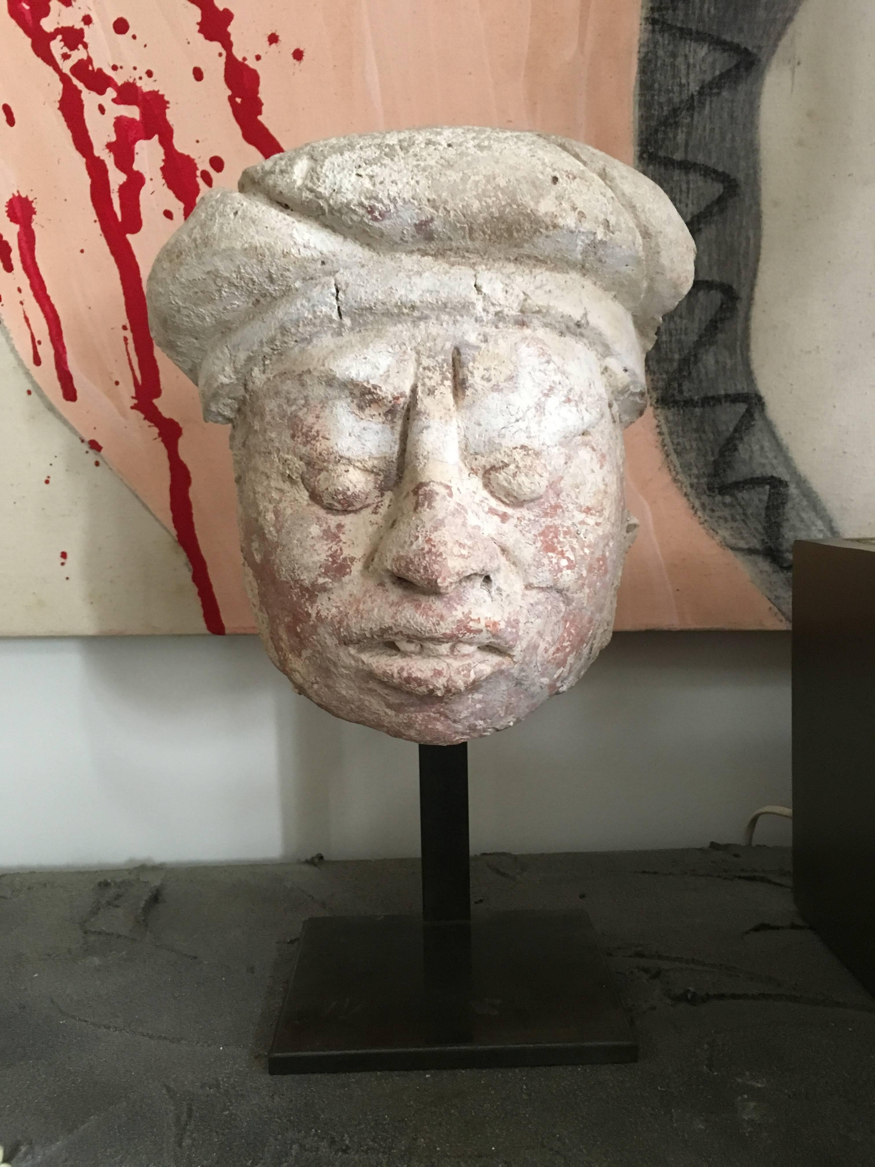 A Mayan Stucco head
Late Classic, ca. A.D. 550-950
The strongly expressive representation marked by tapering orb eyes, the ridge of the nose extending up and through the frowning brow, with fleshy cheeks and open mouth showing teeth, wearing a
