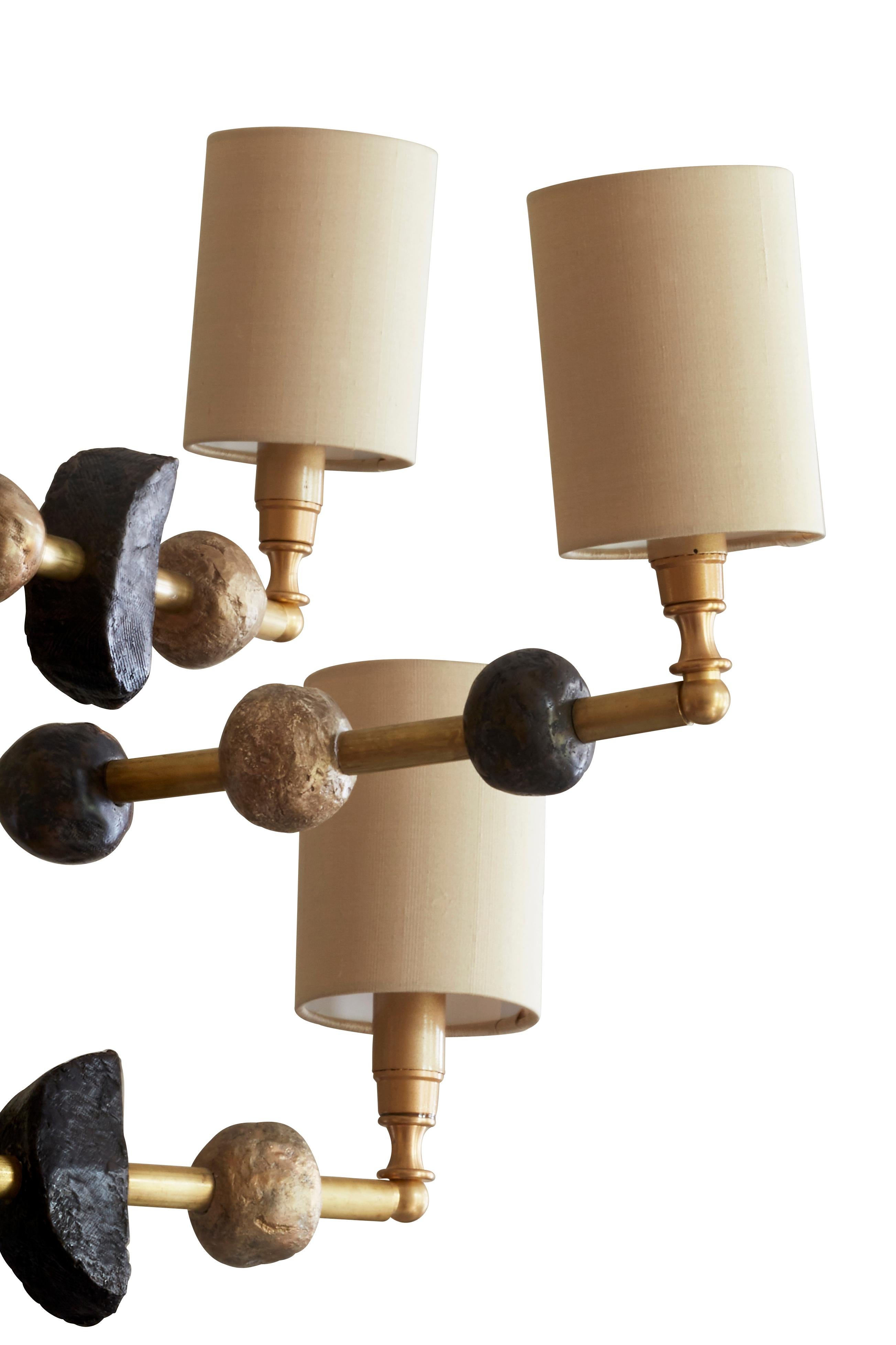 This contemporary three-tier chandelier by Margit Wittig features sculptural components with organic and subtle textures, all cast and treated with multiple layers of patina in her London studio. The contrast of dark, gold-waxed resin and brass, is
