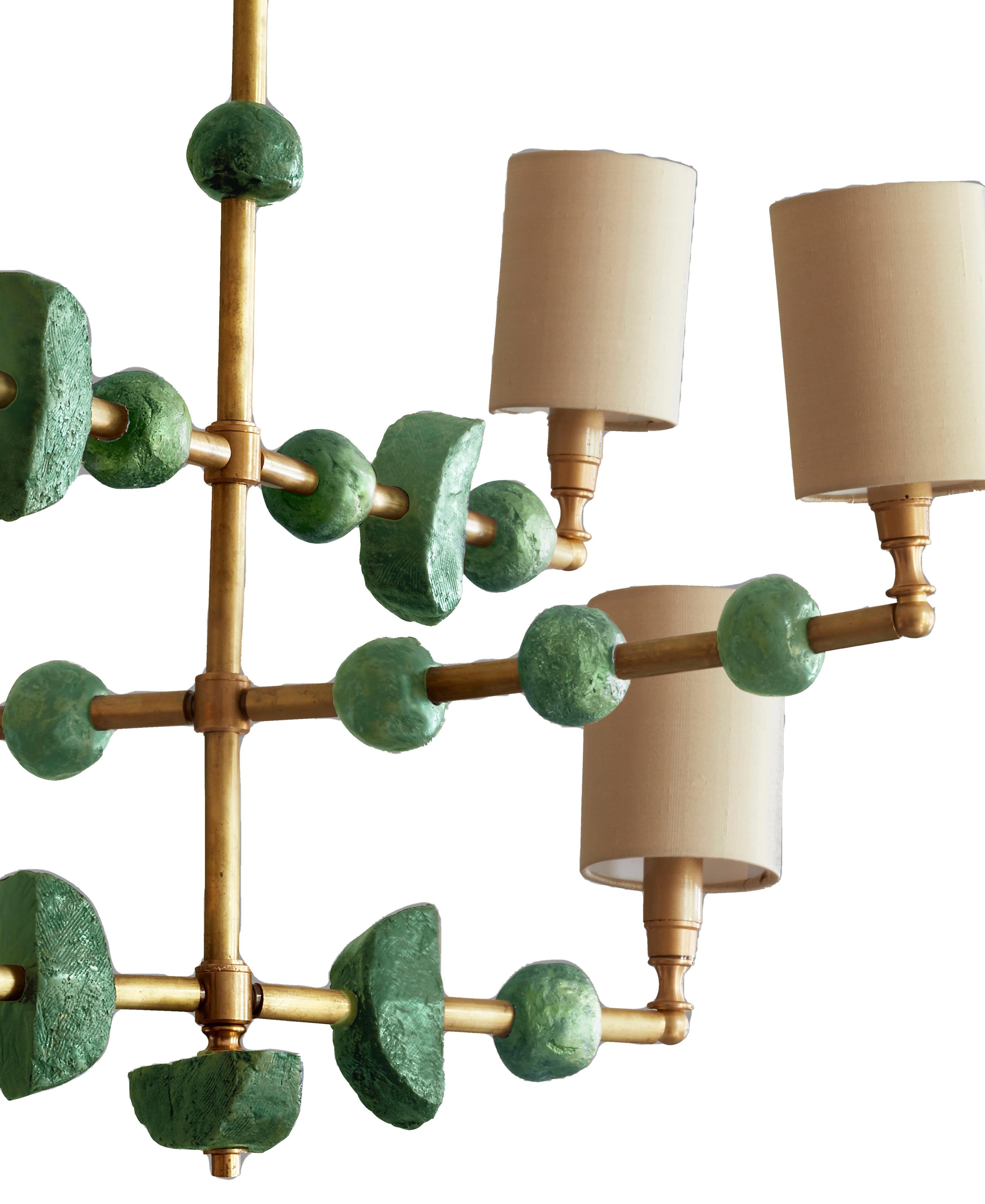 This contemporary three-tier chandelier by Margit Wittig features sculptural components with organic and subtle textures, all cast and treated with multiple layers of patina in her London studio. The contrast of green waxed resin and brass, is the