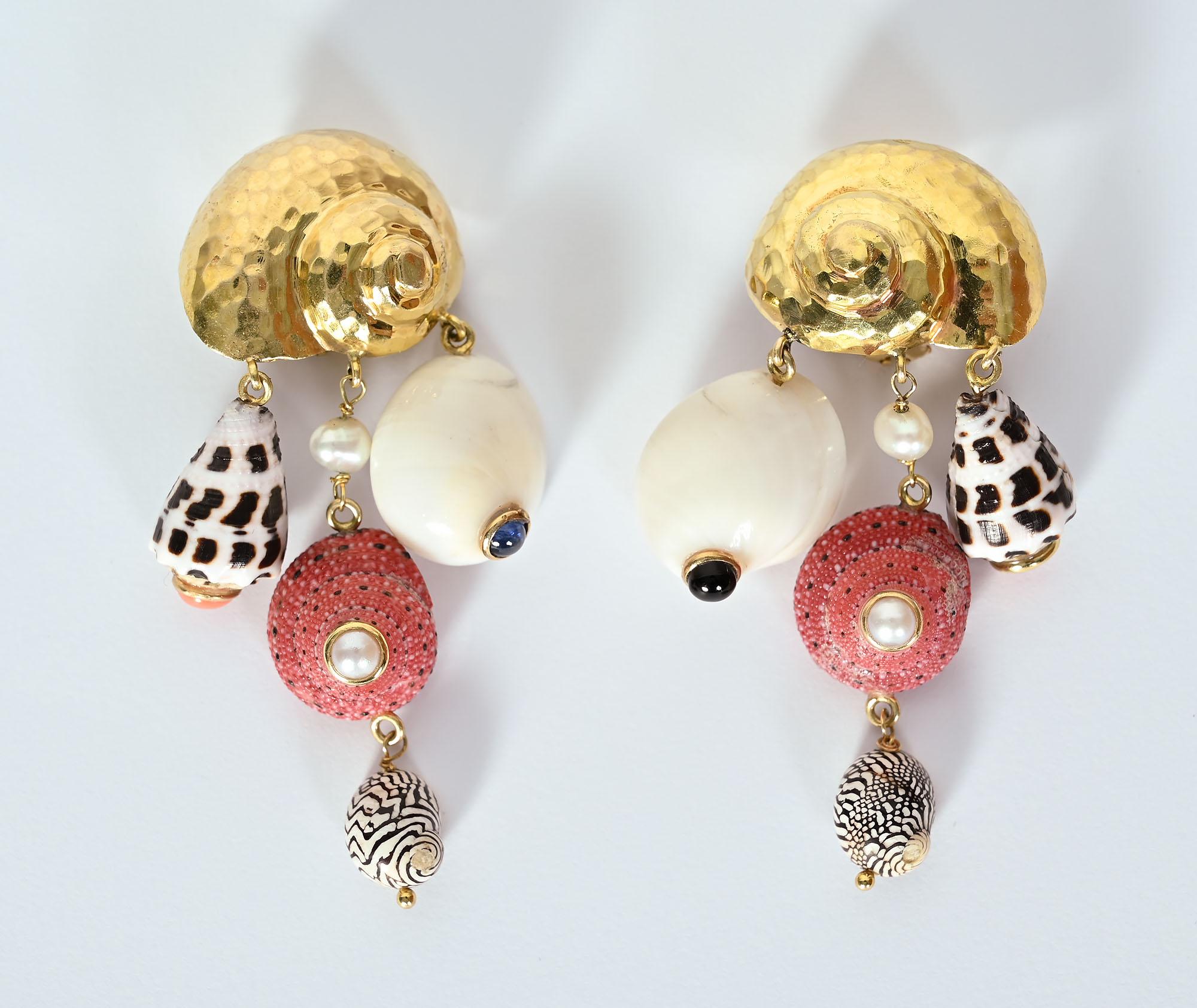 Charming and playful gold shell earrings from which four actual shells are suspended. The gold shell has a hammered finish. The middle shell has a pearl above it and inserted in its middle. The white shells are each centered with a cabochon