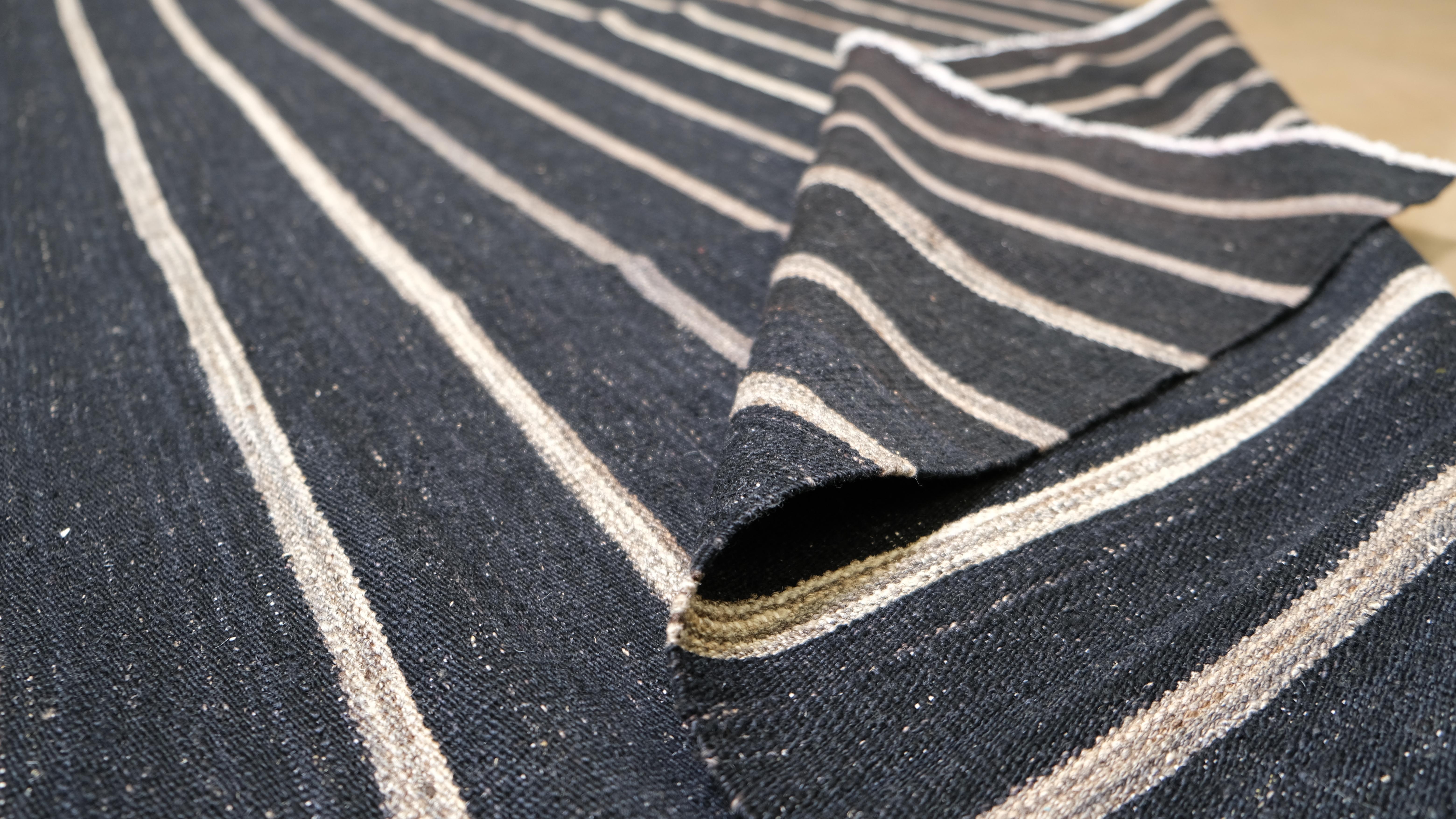Eleva il tuo spazio con il design elegante e moderno di questo kilim in lana intrecciata a mano. Con un'audace base antracite accentuata da strisce avorio uniformemente distanziate, questo tappeto combina semplicità e raffinatezza. Il suo