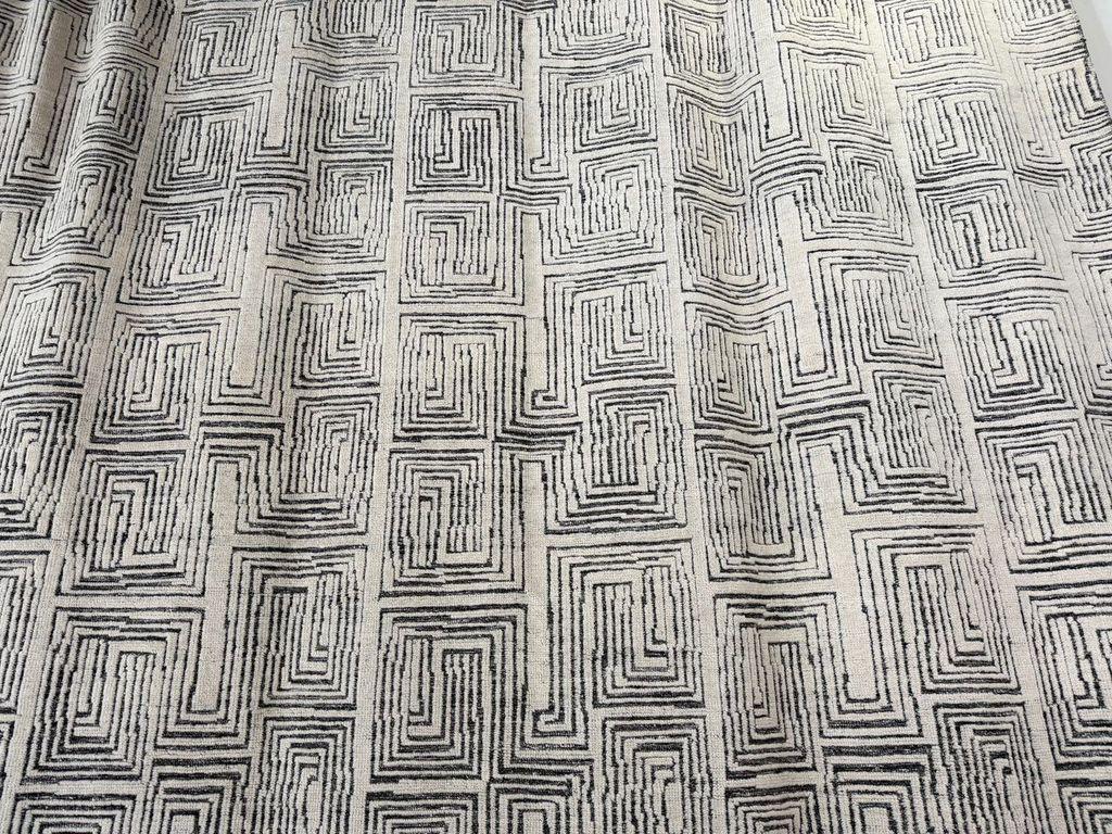 Tapis indien à motifs de labyrinthes, d'une grande douceur, en ivoire et anthracite, fait de laine et de viscose. Ses motifs détaillés et répétitifs attirent l'attention.