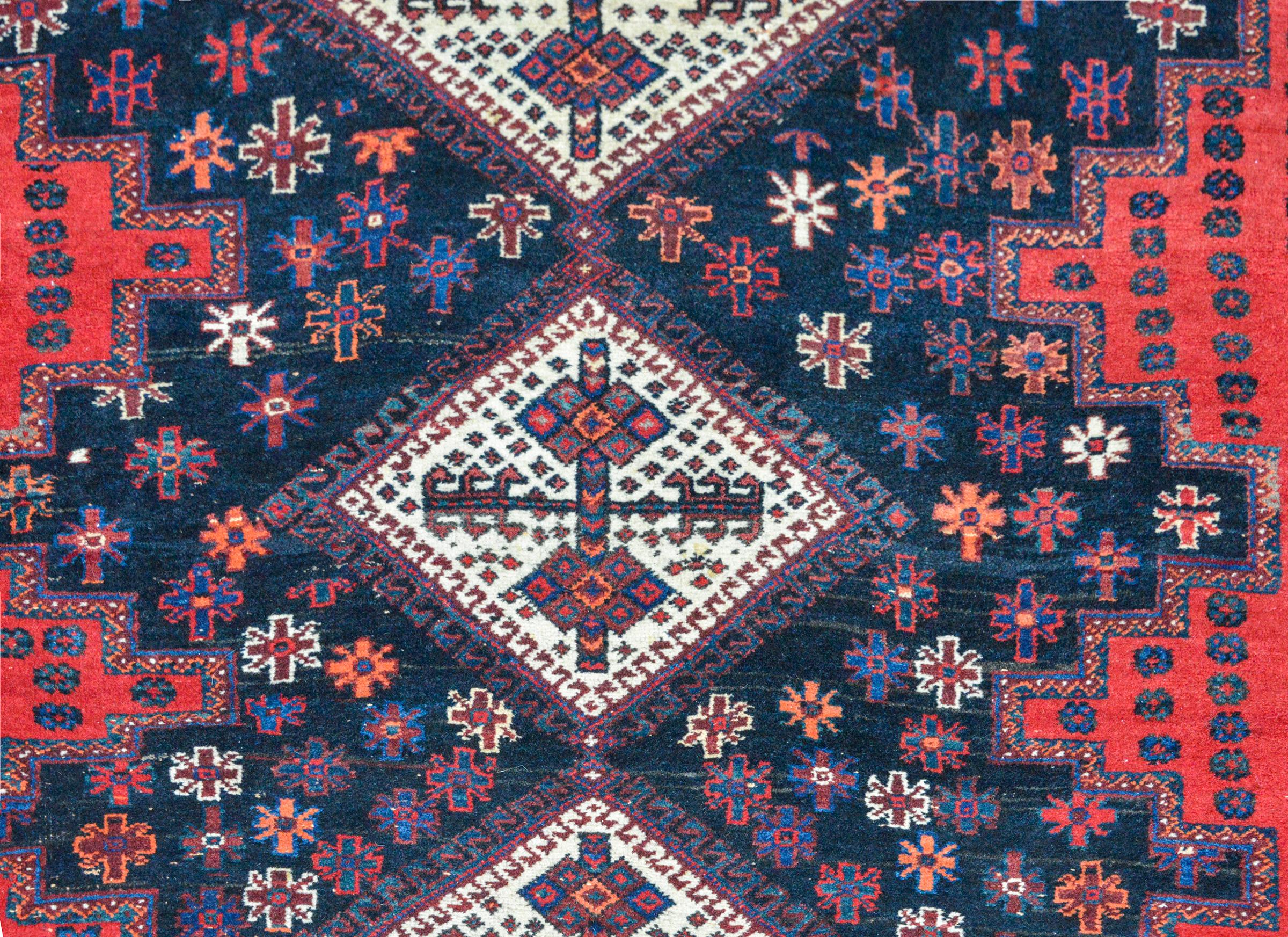 Vintage Persian Mazlaghan rug with a bold geometric pattern woven with three large white diamond medallions amidst a field of stylized flowers against a dark indigo background. The border is striking, with multiple petite and large-scale geometric