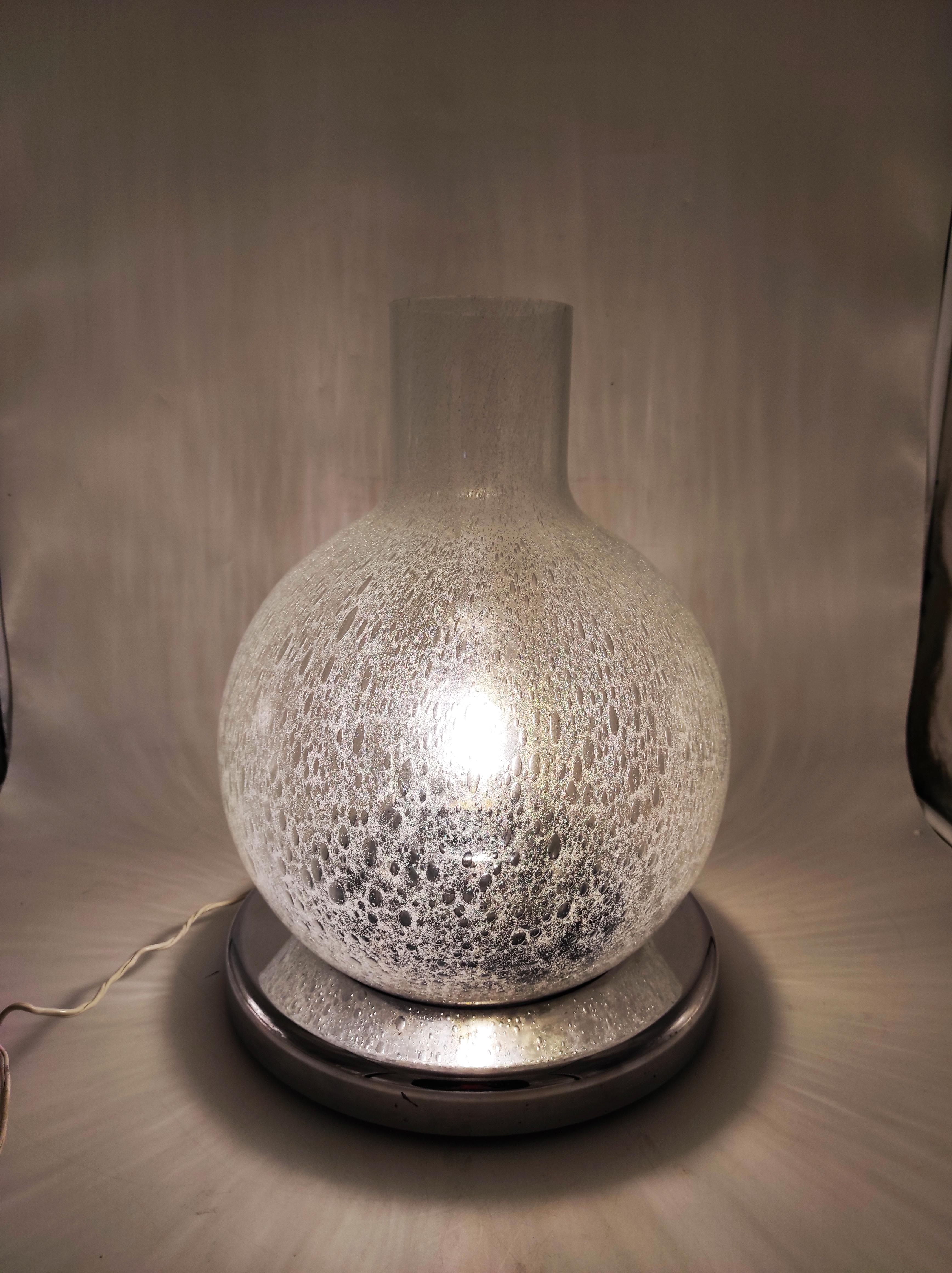 Prächtige italienische Tischlampe aus Pulegoso Murano Glas und verchromtem Metall.
Die aus den 1970er Jahren stammende Leuchte erinnert in Design und MATERIAL an die Produktionen des historischen venezianischen Unternehmens 