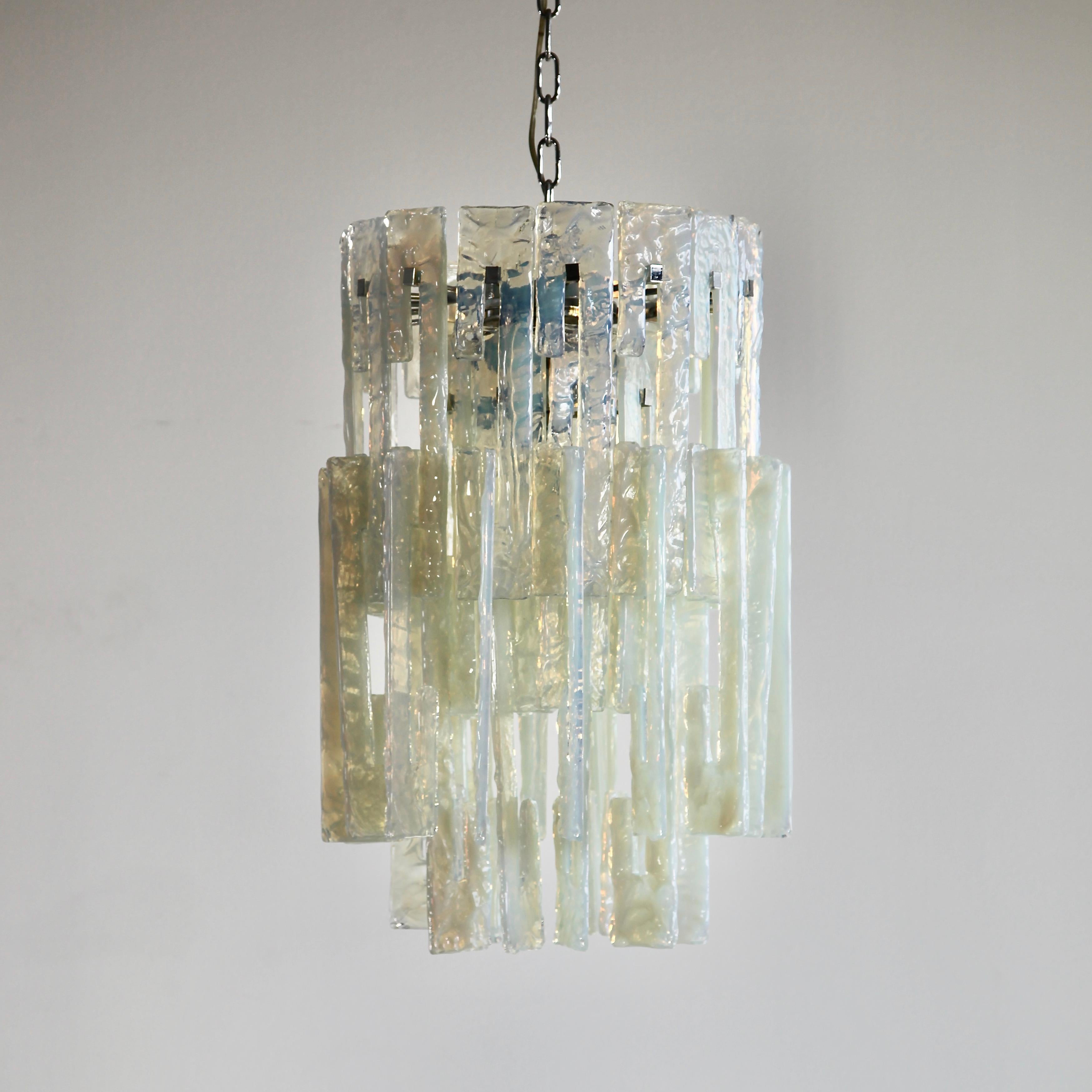 Glass Chandelier by Mazzega. Italy, Murano 1960s.

Vintage hanging lamp comprising of a metal frame and some 52 interlocking glass pieces, hand-made in Murano. Rare chandelier with interlocking opal glass pieces with a hint of green colour. Four