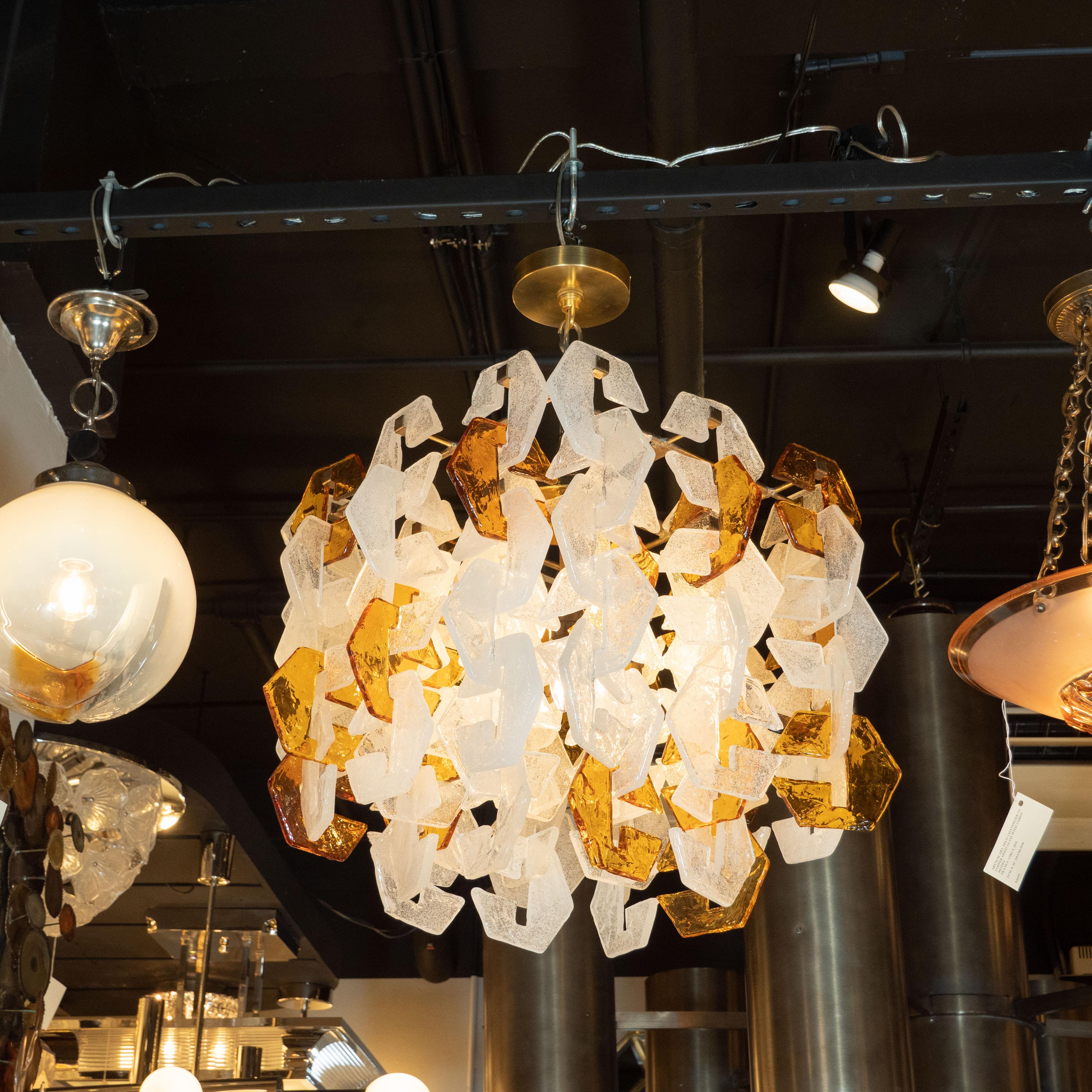 This stunning Mid-Century Modern chandelier was realized by the fabled Italian glass studio, Mazzega, in Murano, circa 1970. It features an abundance of interlocking three-sided geometric glass shades in translucent amber and semi opaque white glass