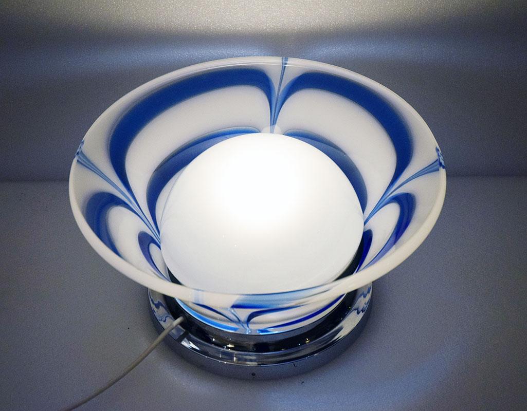 
Table lamp produced by Mazzega Murano in the 70s.
Chromed steel base with double blown glass diffuser.
One white glass with blue inserts and one in satin glass.
In excellent condition.

Dimensions: diam 43 x h 23 cm