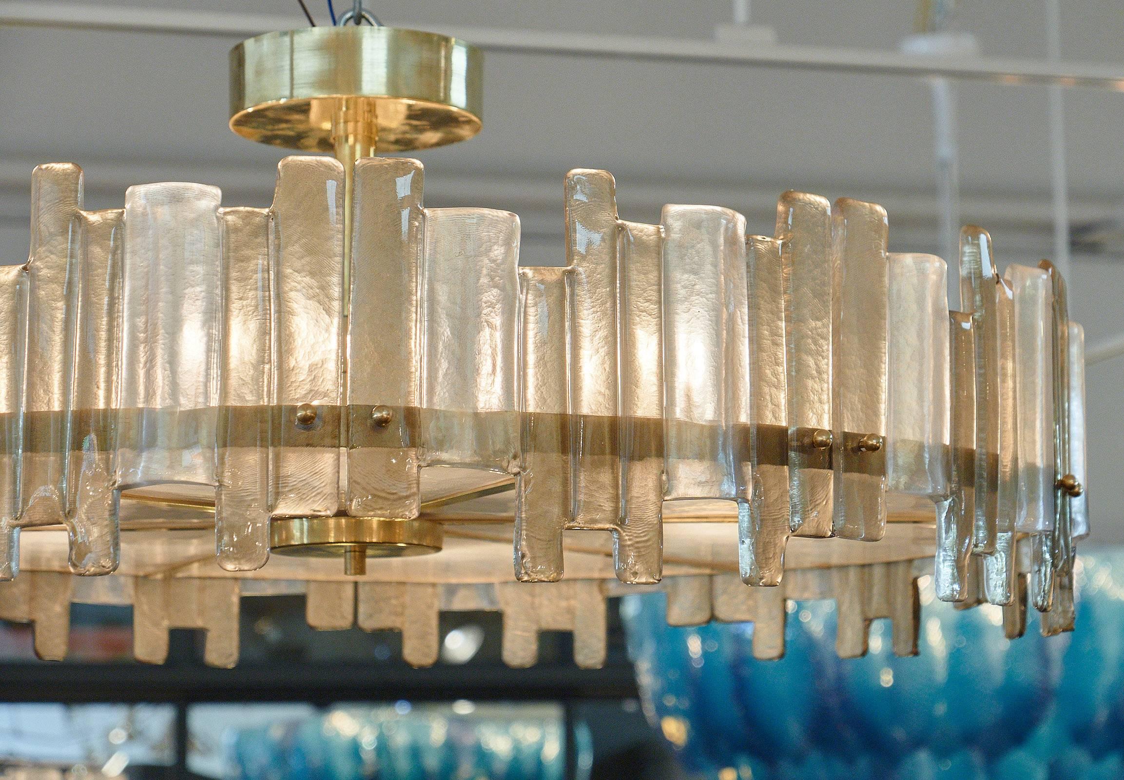 Spektakulärer Mazzega-Kronleuchter aus Muranoglas in runder Form. Diese Leuchte, die Mazzega zugeschrieben wird, hat organisch geformte, dicke Glaslamellen, die sich in Rauch- und Klarglasfarben um eine massive Messingstruktur abwechseln. Das