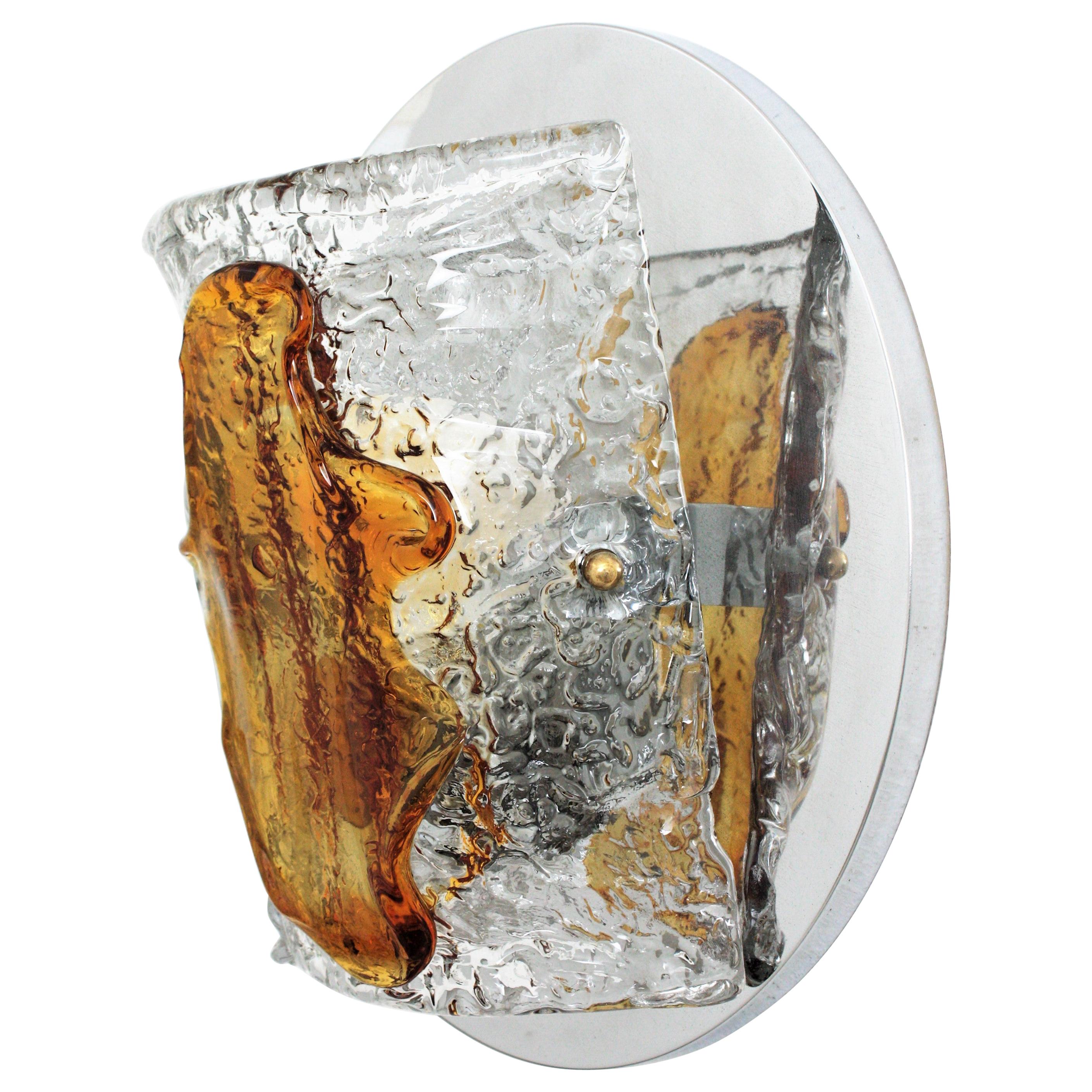 Elegant hand blown amber and clear Murano glass wall sconce by Mazzega, Italy, 1960s.
This beautiful wall light features a circular chromed steel backplate holding a half-cylinder glass shade in textured clear and amber glass.
This light fixture