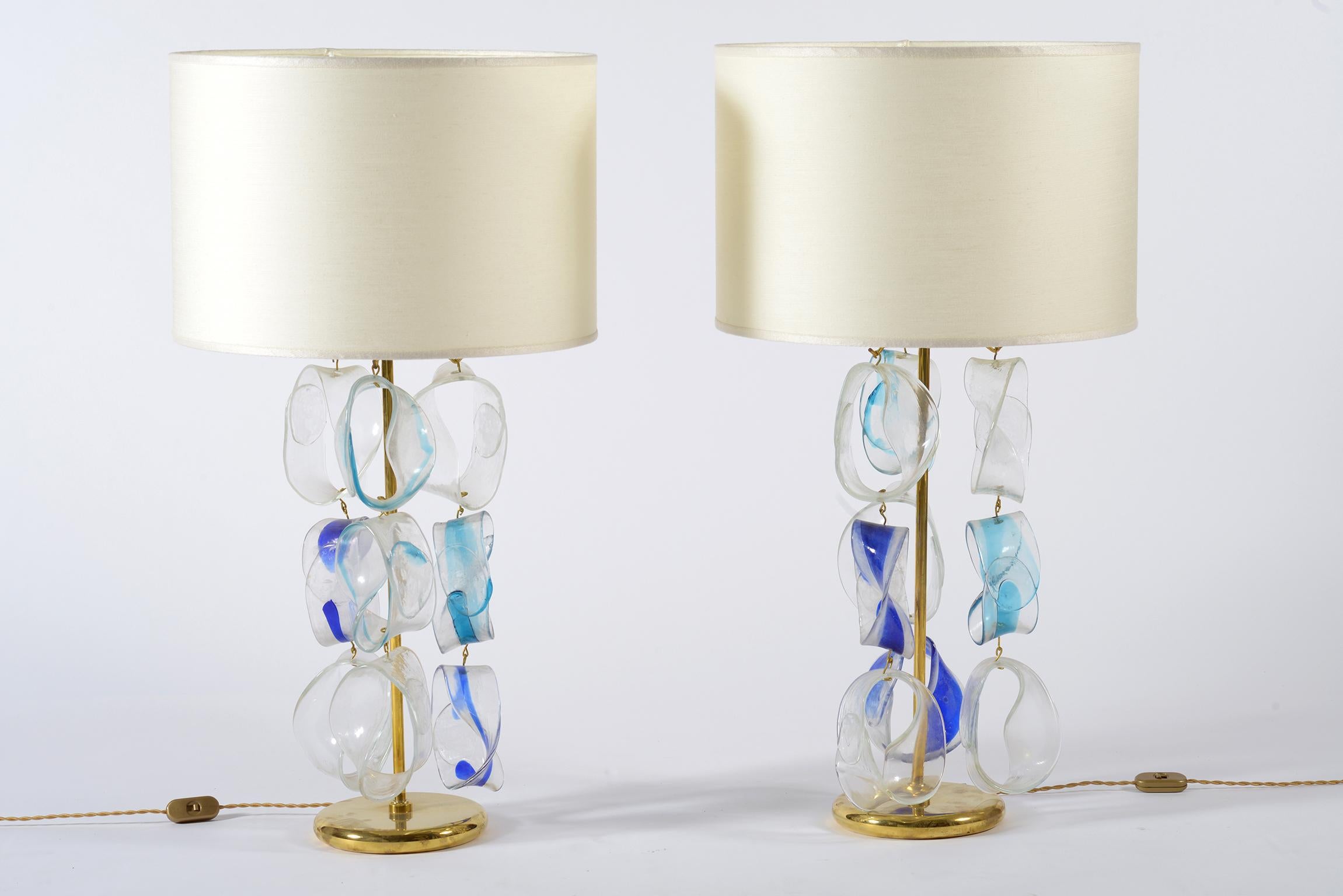 Pair of Murano glass table lamps made by the Mazzega manufactory with chains in transparent glass and blue brass.
The shades are new in light beige silk.
The measures are with lampshades.
Italia midcentury, 1960.