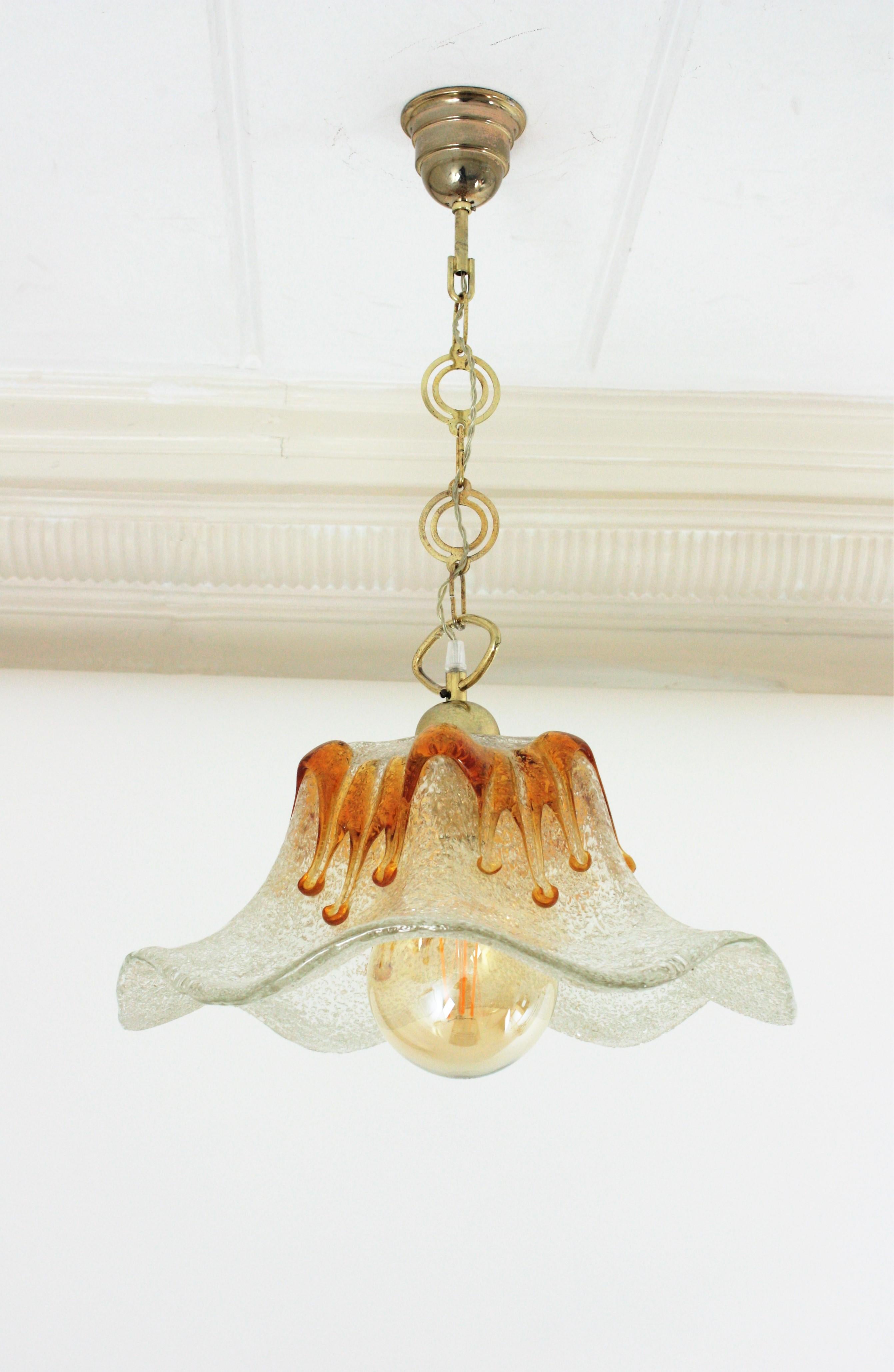 Tulip shaped pendant light by Mazzega Murano, Italy, 1960s.
Italian Mazzega flower shape pendant ceiling light with textured amber and clear glass lampshade. This suspension lamp hangs from a chain with brass links topped by a brass canopy.
The