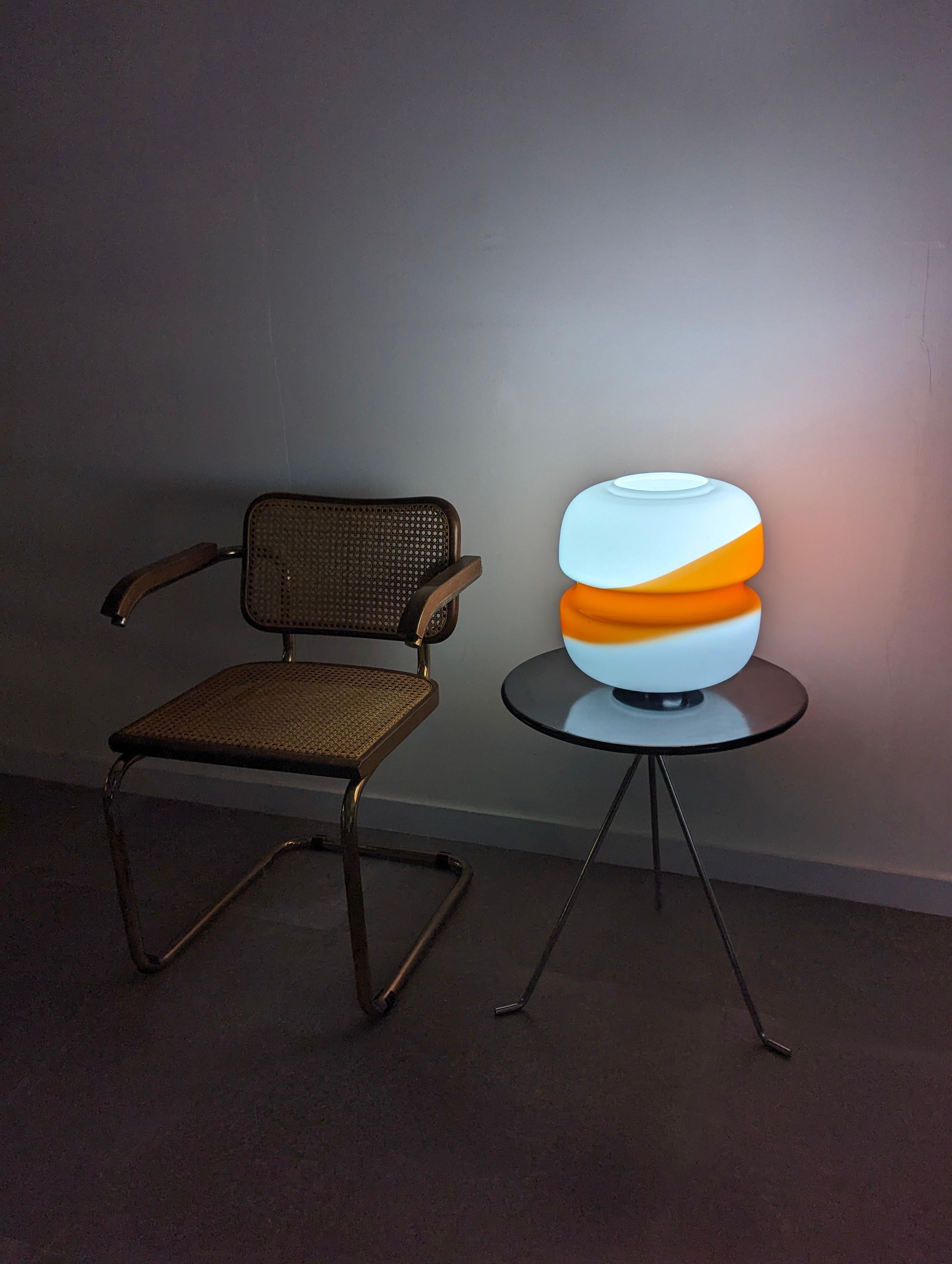 Italian table lamp by Mazzega made in the 70s in white and orange glass with a striking transversal line design. Once turned on, its colors provide a warm and elegant atmosphere.