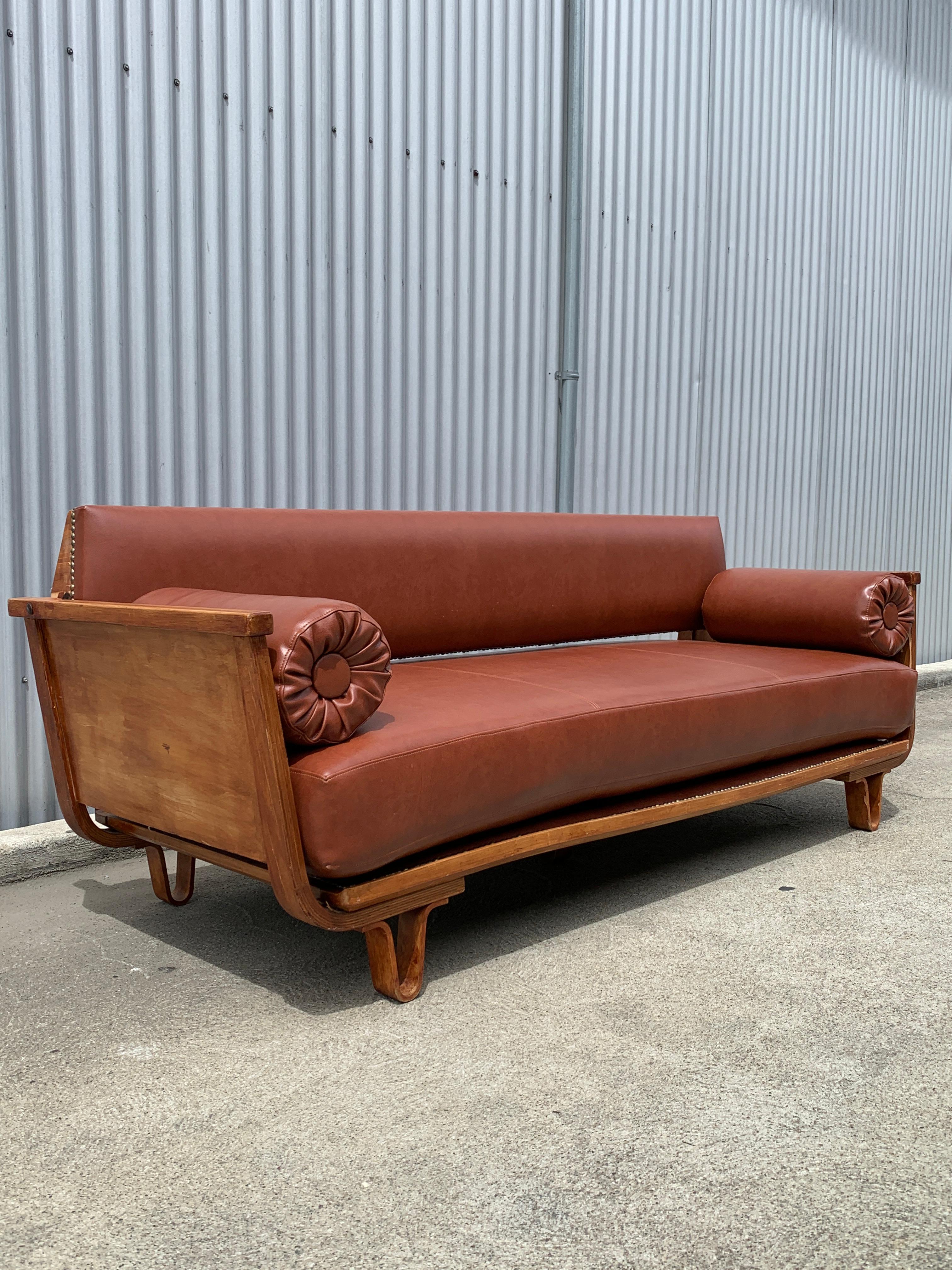 Cees Braakman for Pastoe, Daybed MB01, in a curved birch plywood and red leather. This piece is offered in as-is condition with a more victorian feel; a darker stain and nailhead trim. No structural damage can be found, and the piece works as